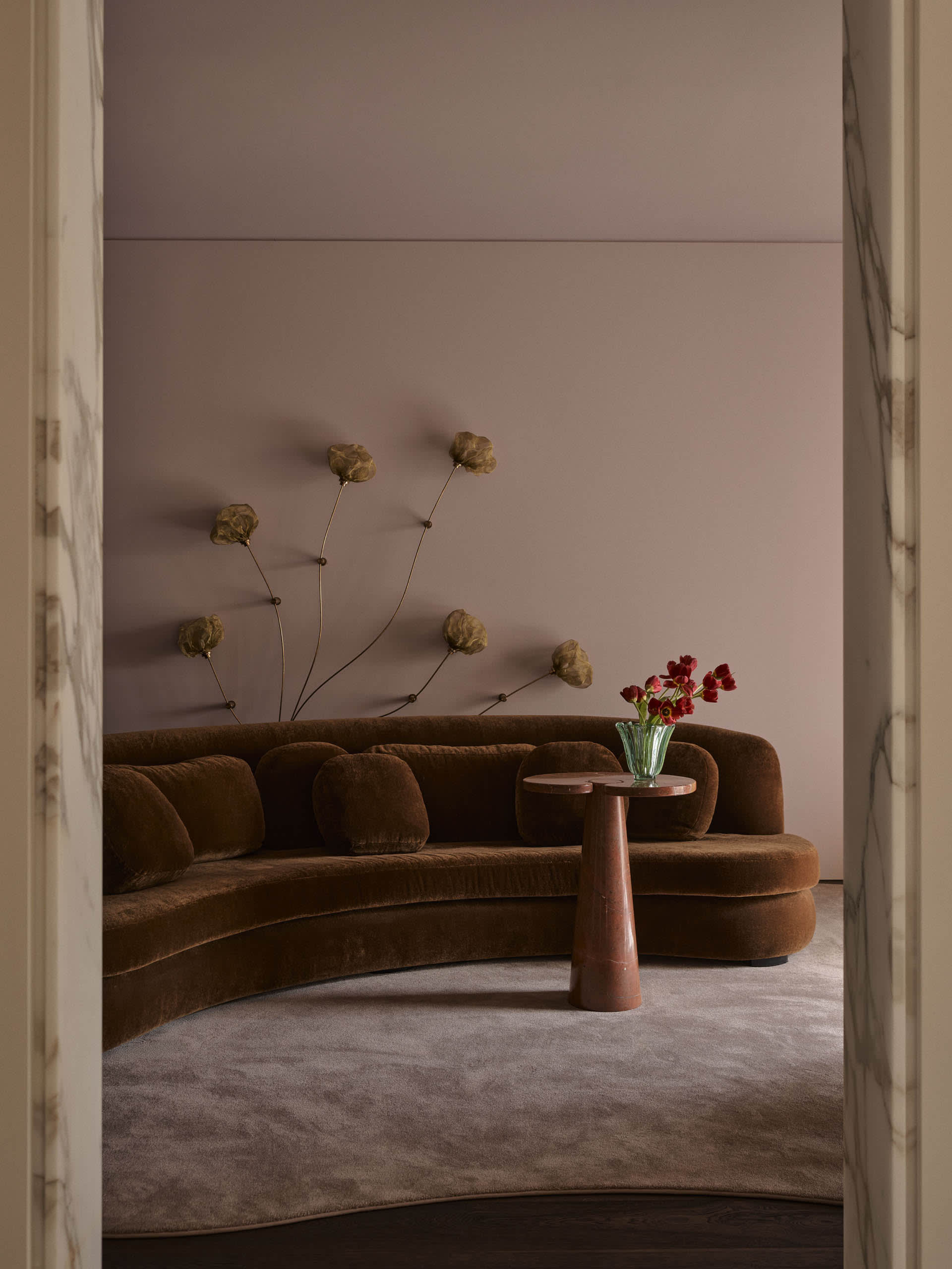 Cozy modern living room with a brown couch and chair, a vase with flowers on a table, and dim lighting