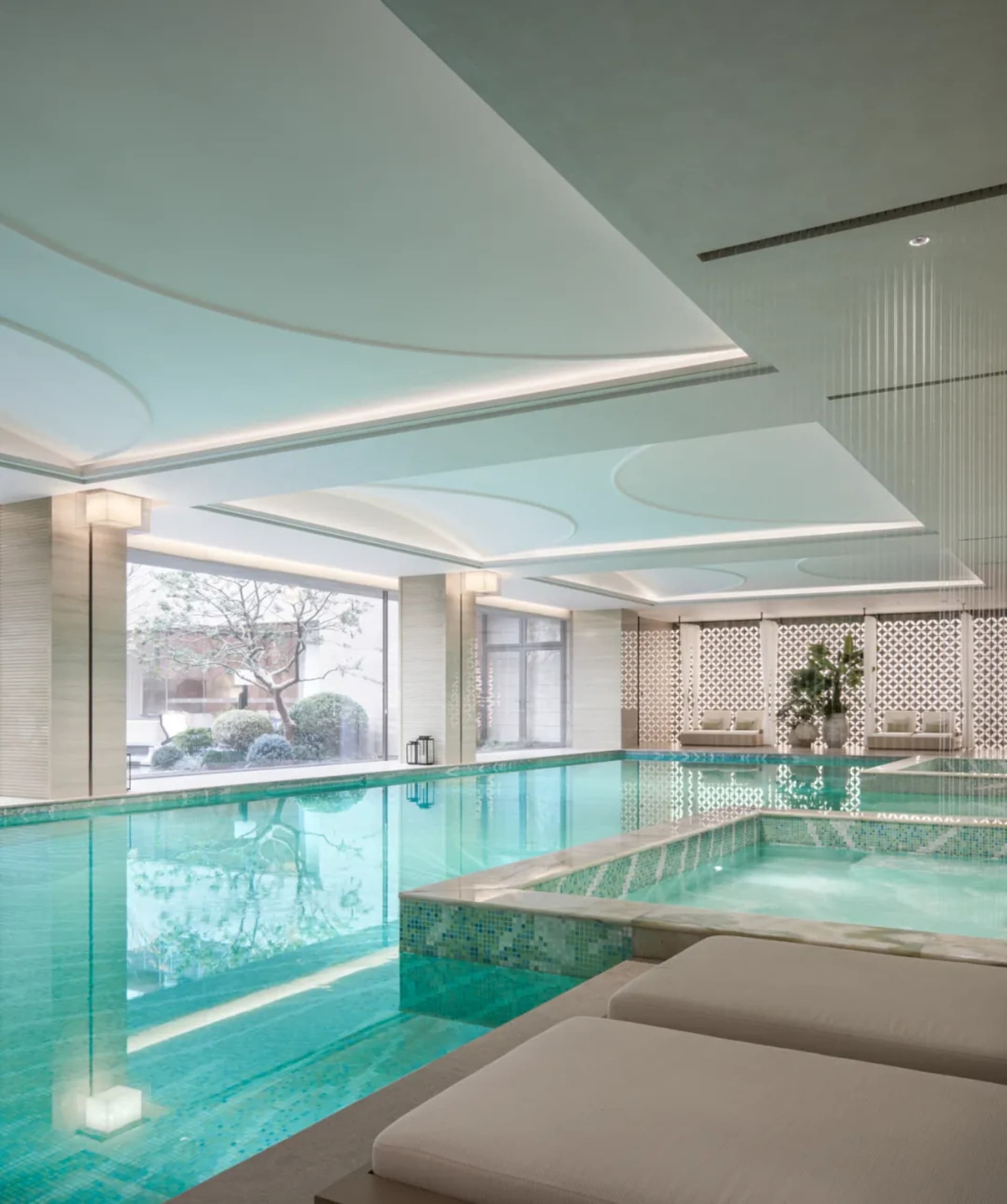A modern pool area with a white tiled space, a white couch, and a well-lit pool surrounded by water