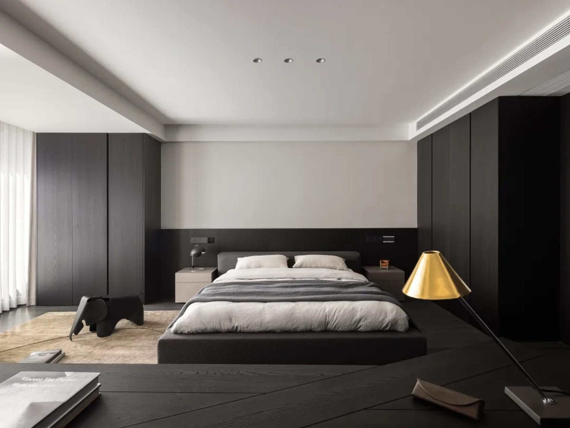 A dimly lit hotel bedroom with a black bed, chair, and gold lamp, creating a cozy atmosphere