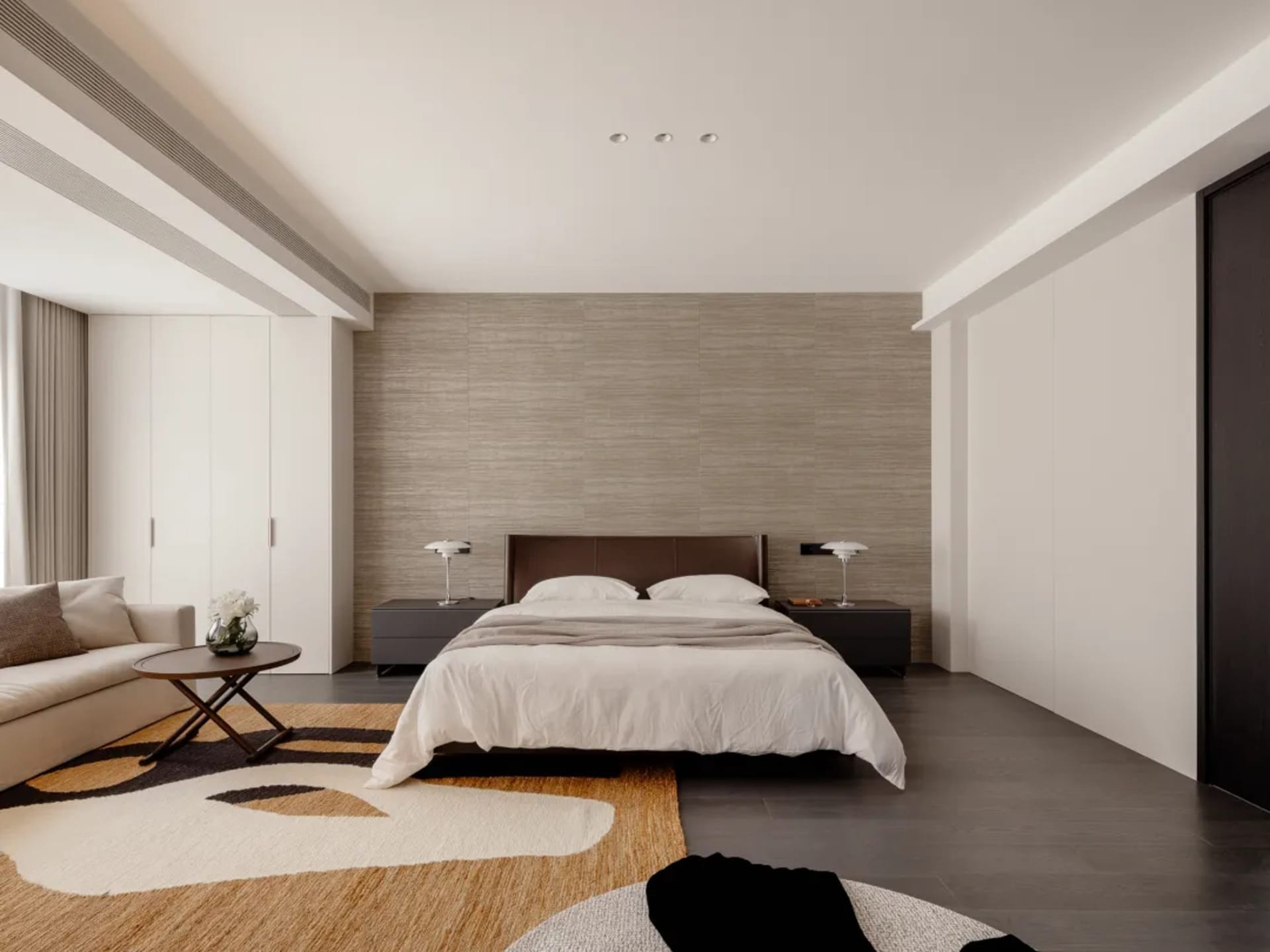 Cozy modern bedroom with a bed, chair, and table in a white room with dim lighting and wood furniture