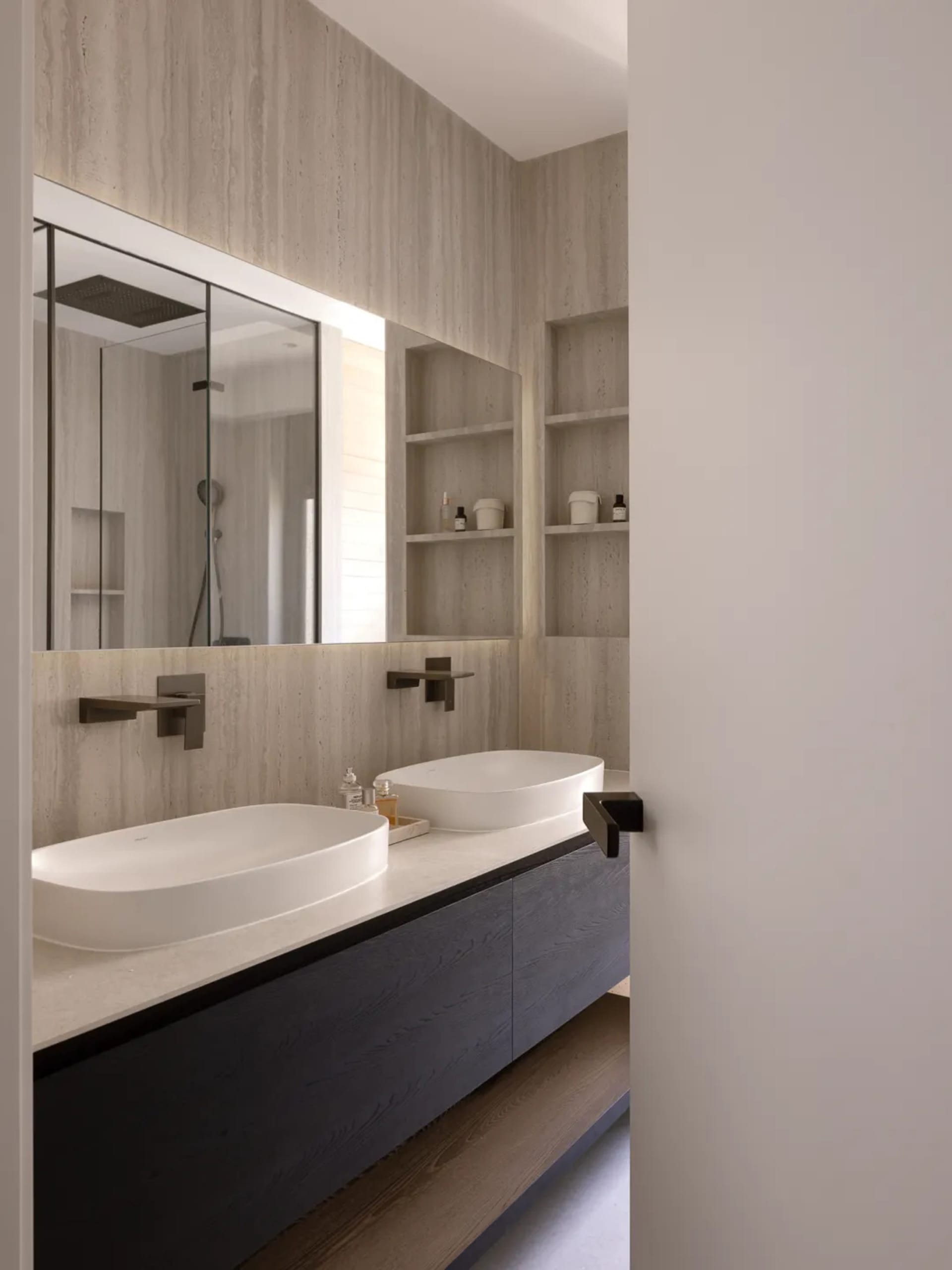 A modern bathroom with a white sink and bathtub, wooden cabinet, and mirror, set in a dimly lit space