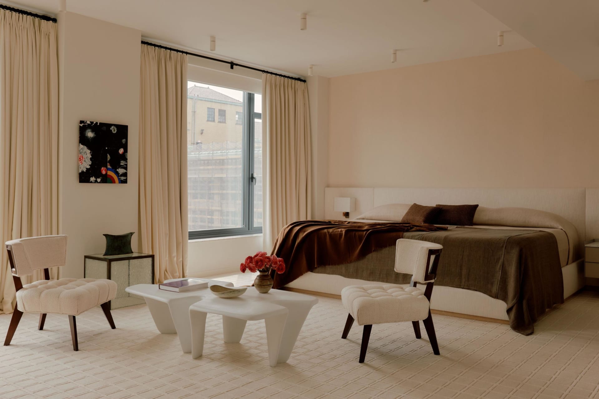 A bedroom with a bed, chair, table, and couch, featuring a large window for natural light and a cozy atmosphere