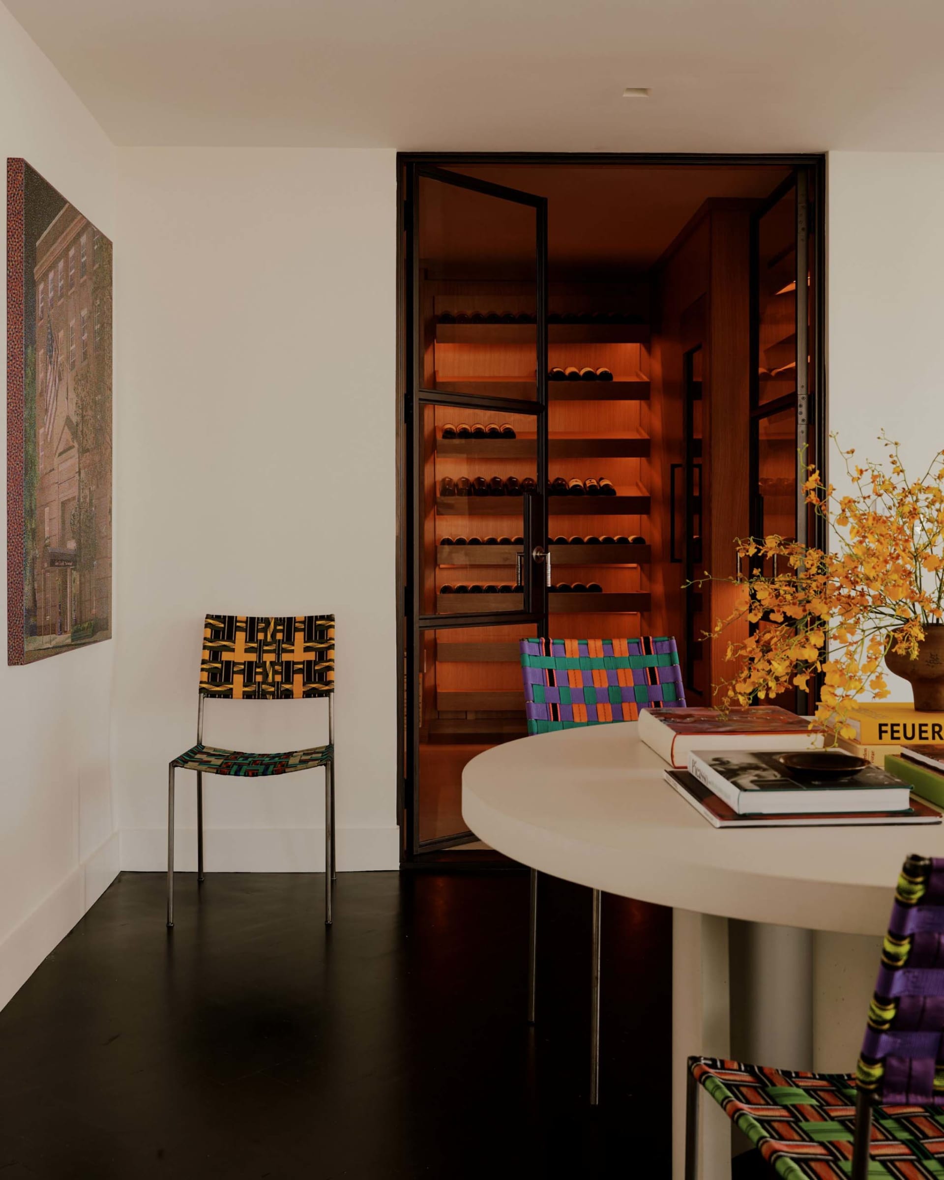 Cozy dining room with a white wall, a dining table, chairs, a potted plant, and a wine rack near the doorway