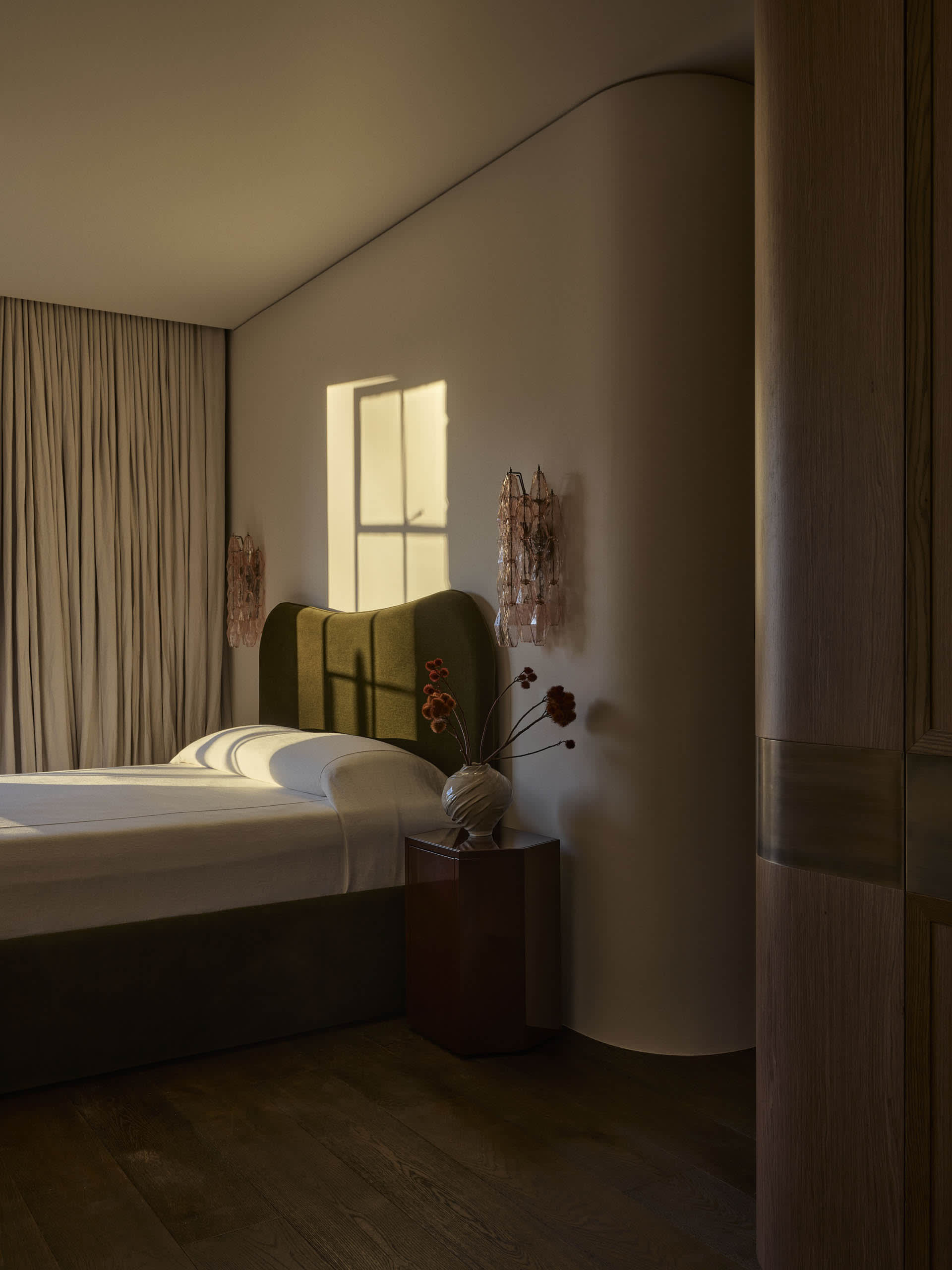 Cozy bedroom with a bed near a window, a vase with flowers on a table, and dim lighting