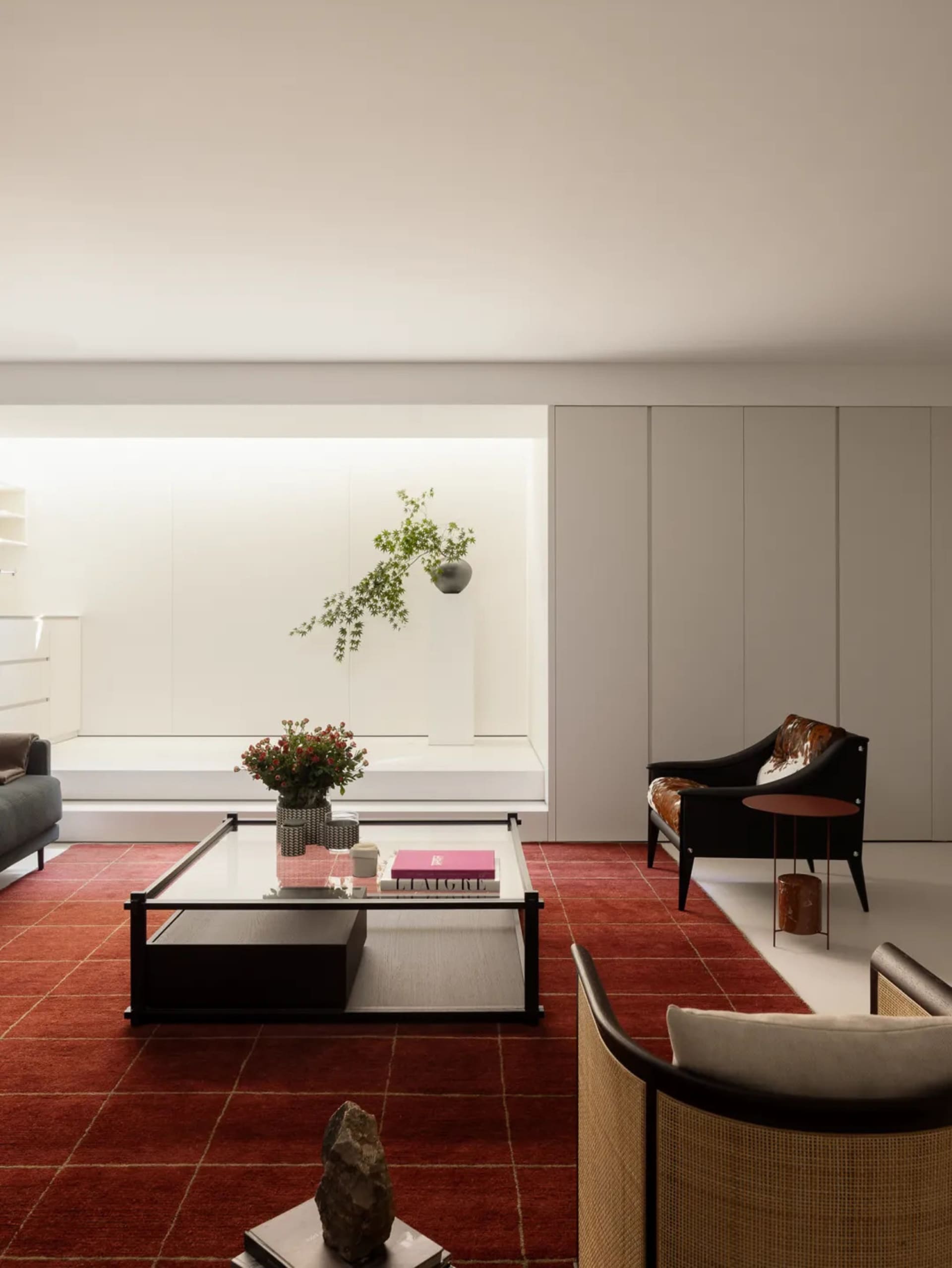 Cozy living room with a red carpet, a couch, a chair, a coffee table, and a potted plant, well-lit with natural light from a window