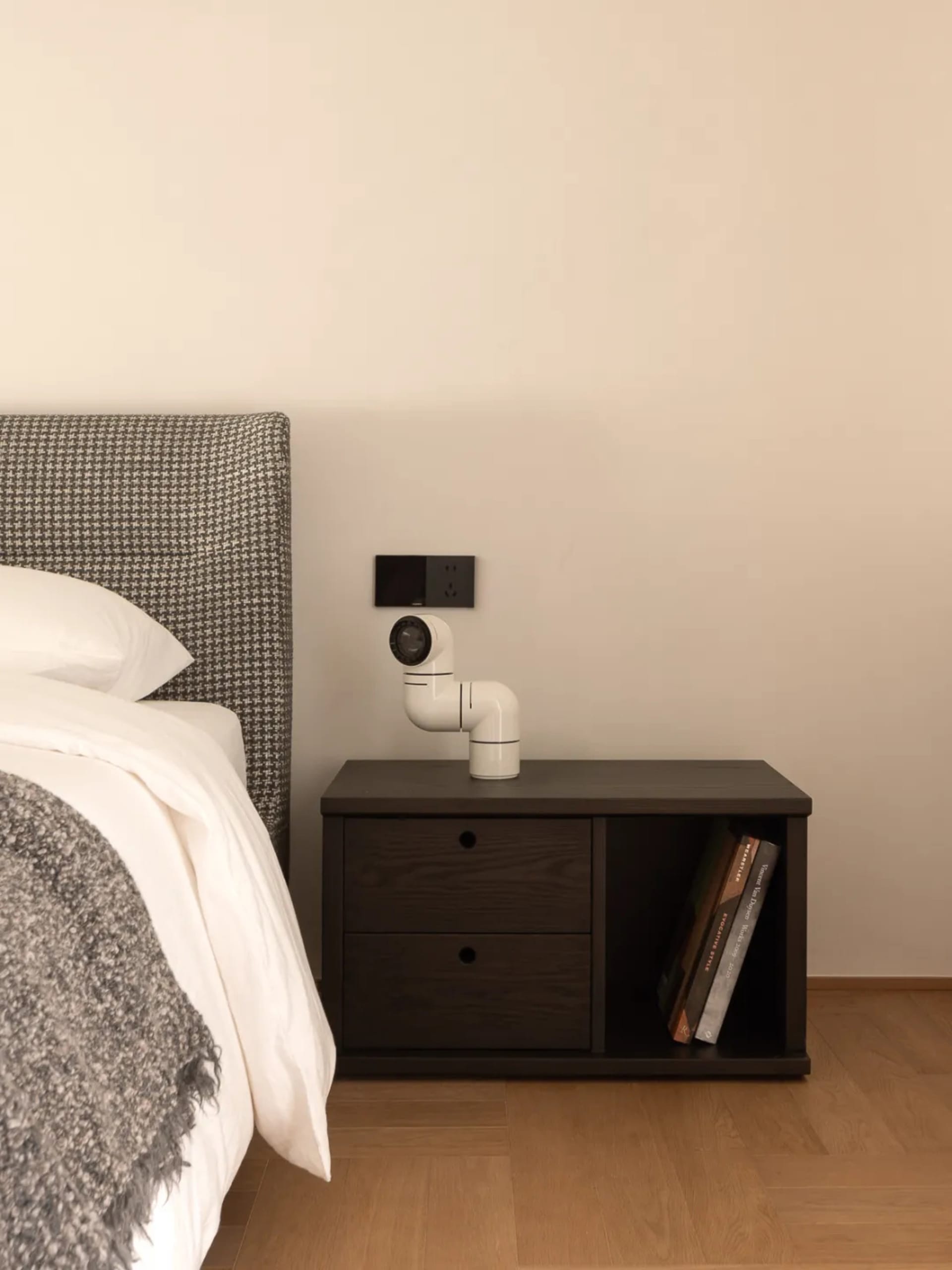 A modern bedroom with a white bed, nightstand, and bookshelf, featuring a clean and bright appearance with natural light and a warm atmosphere