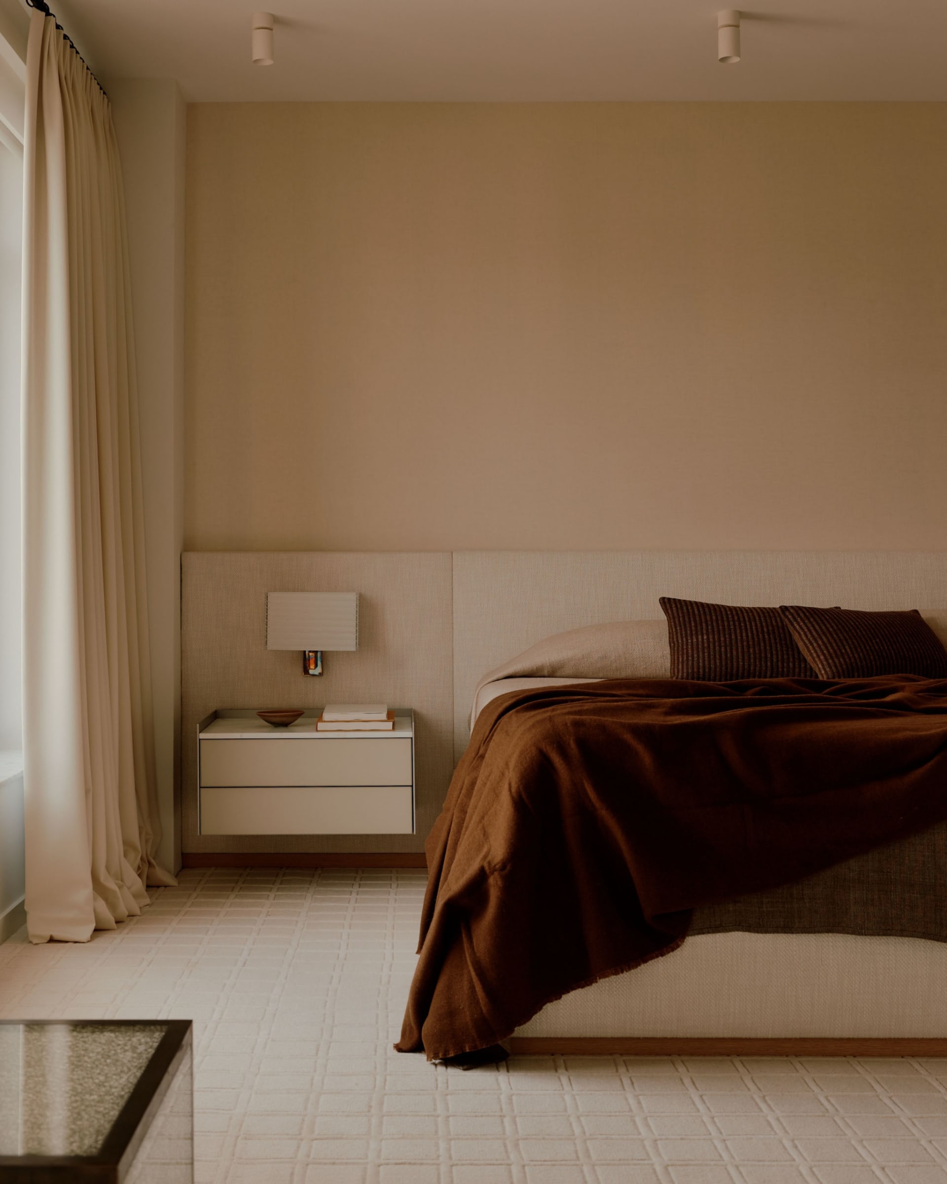 Cozy bedroom with a bed, nightstand, and lamp, surrounded by modern wood furniture and white walls, with natural sunlight coming through the window