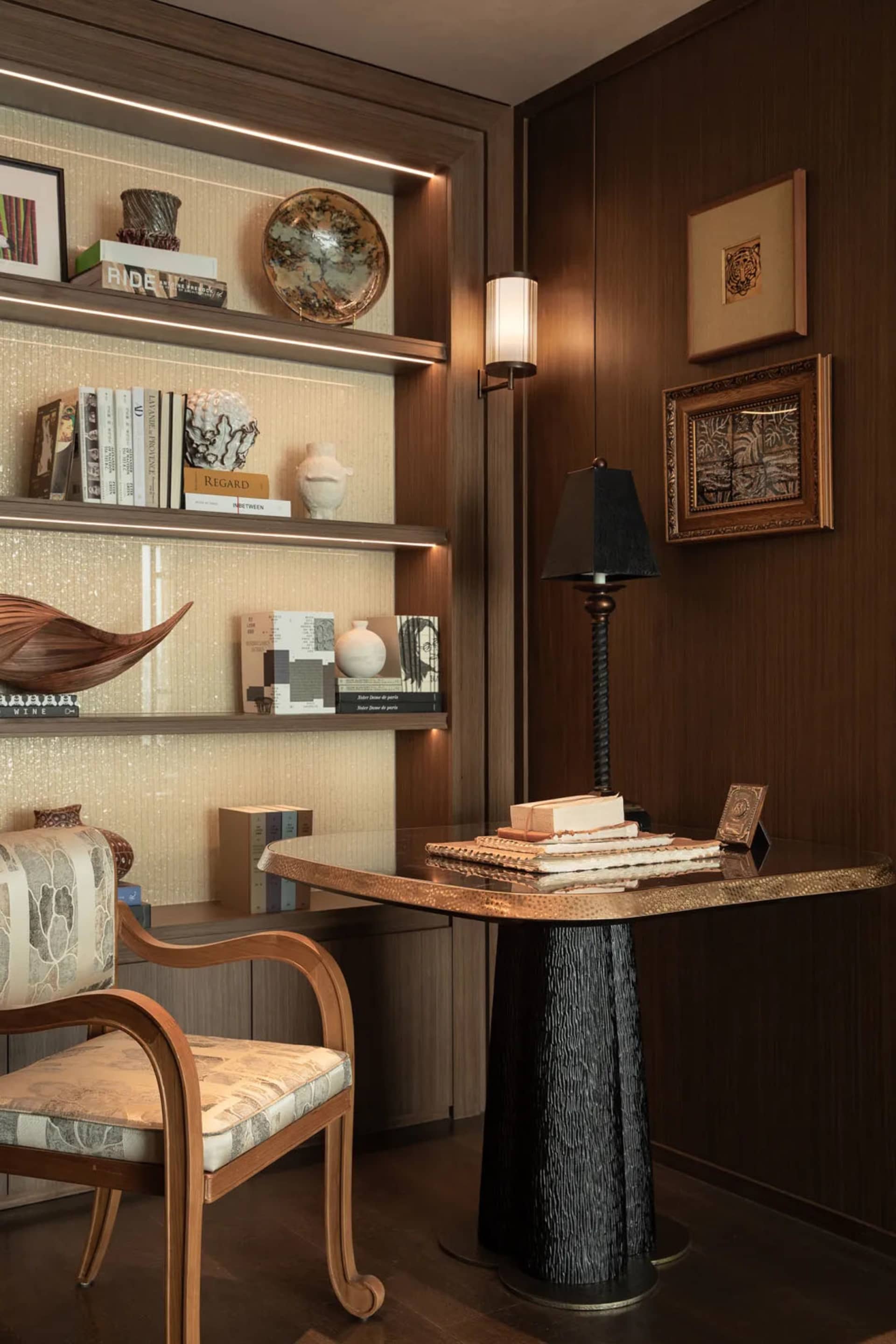 A well-lit living room with a wooden floor, a bookshelf, chair, lamp, and table, featuring a cozy atmosphere and natural light from a window