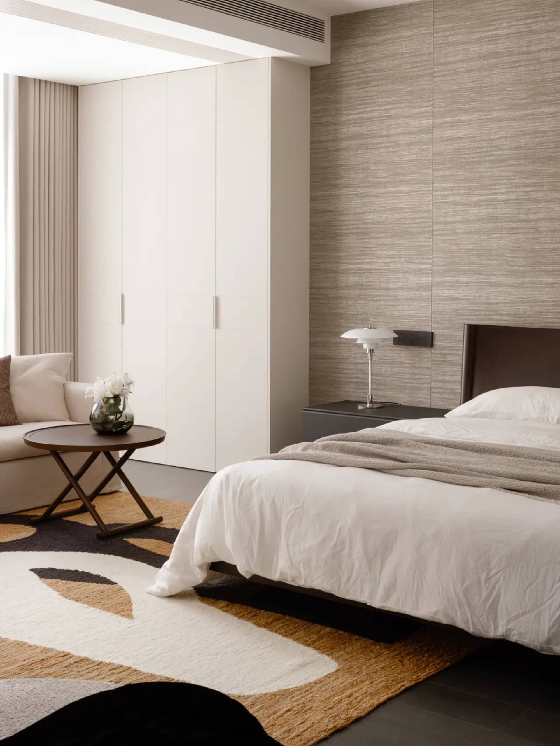 Cozy bedroom with a bed, couch, and table in a white color scheme, with natural light from a window