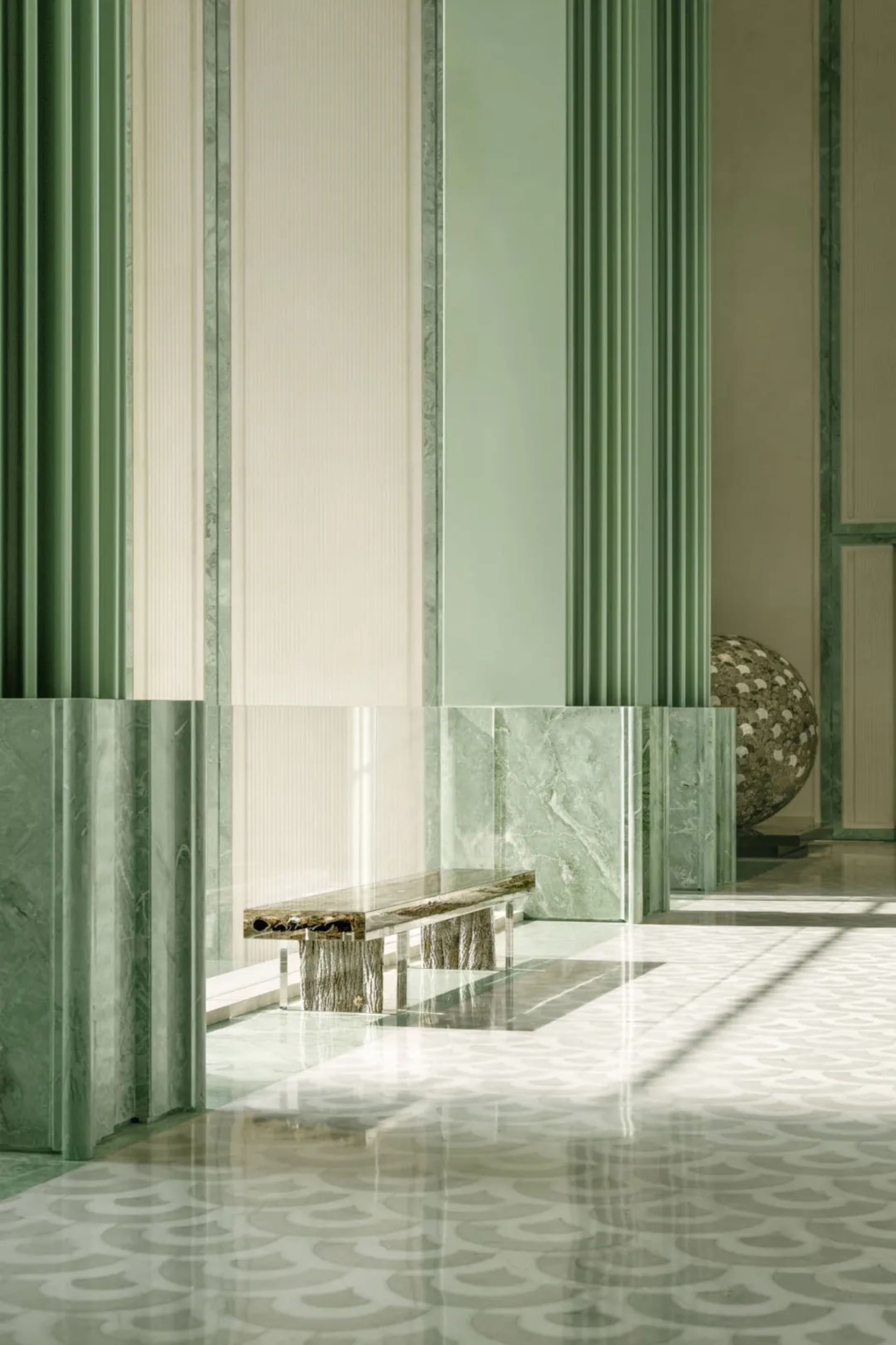A bright and welcoming lobby with green walls, a glass door, a bench, and a dining table, with a vase on the right side