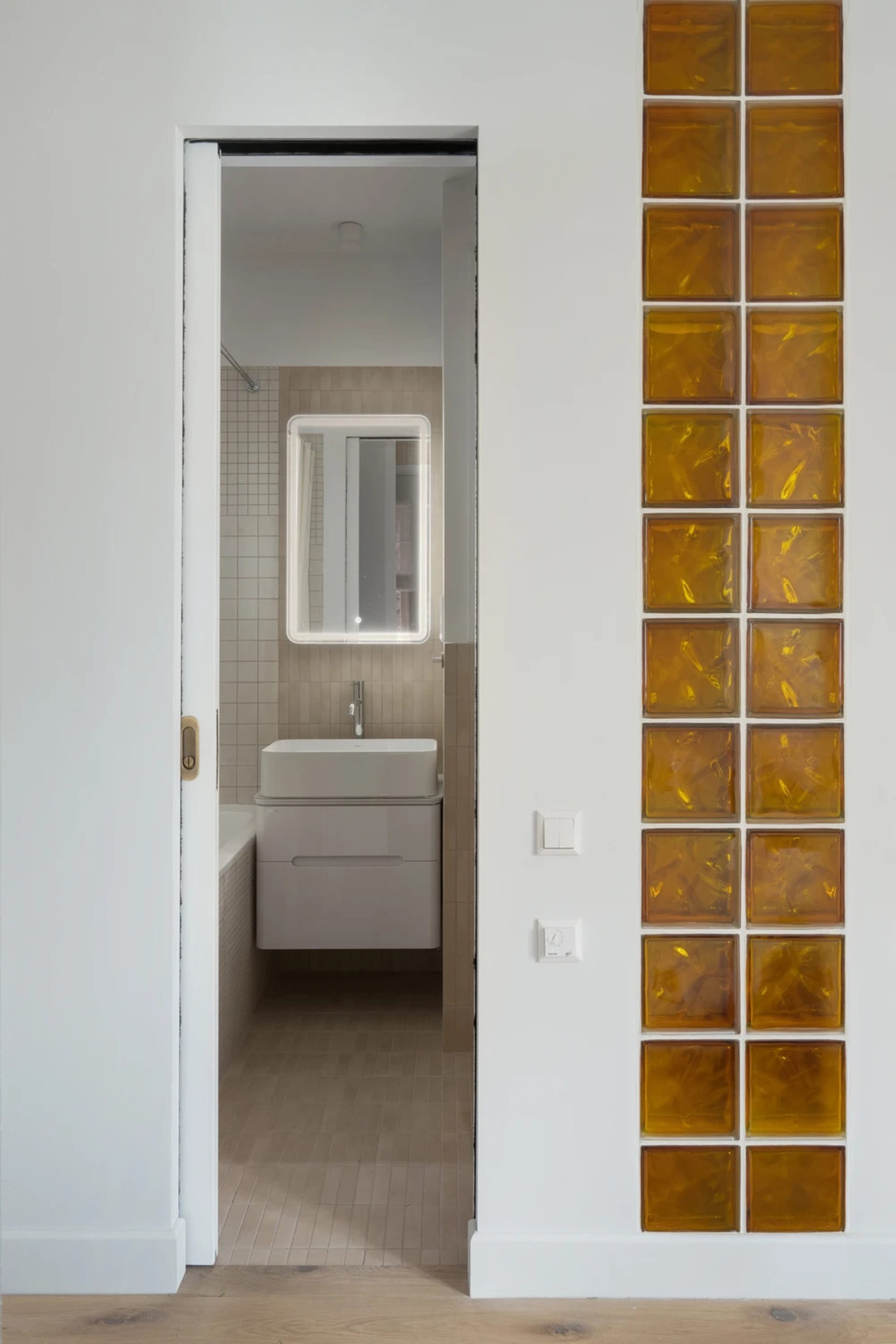 Bathroom with a white sink, mirror, and toilet, set against a tiled background with dim lighting