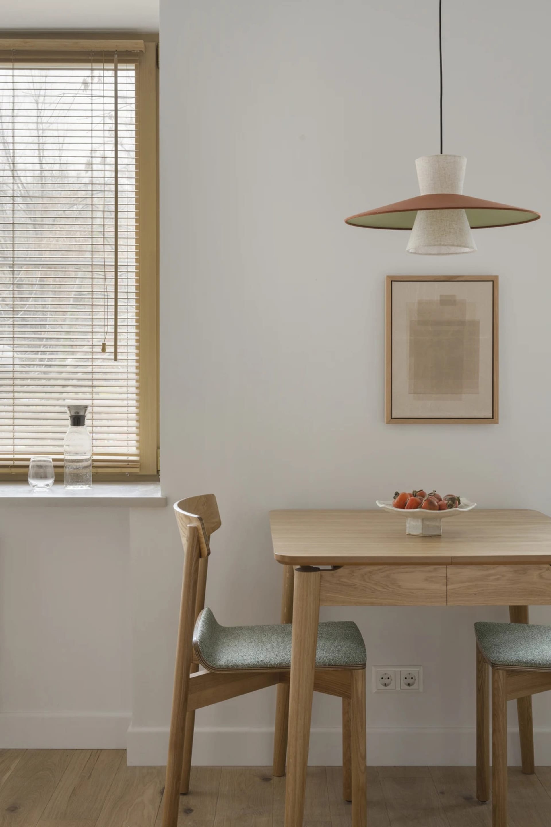 Dining room with a wooden table and chairs, set with a bowl of fruit and a vase, in a bright and inviting space with a white color scheme
