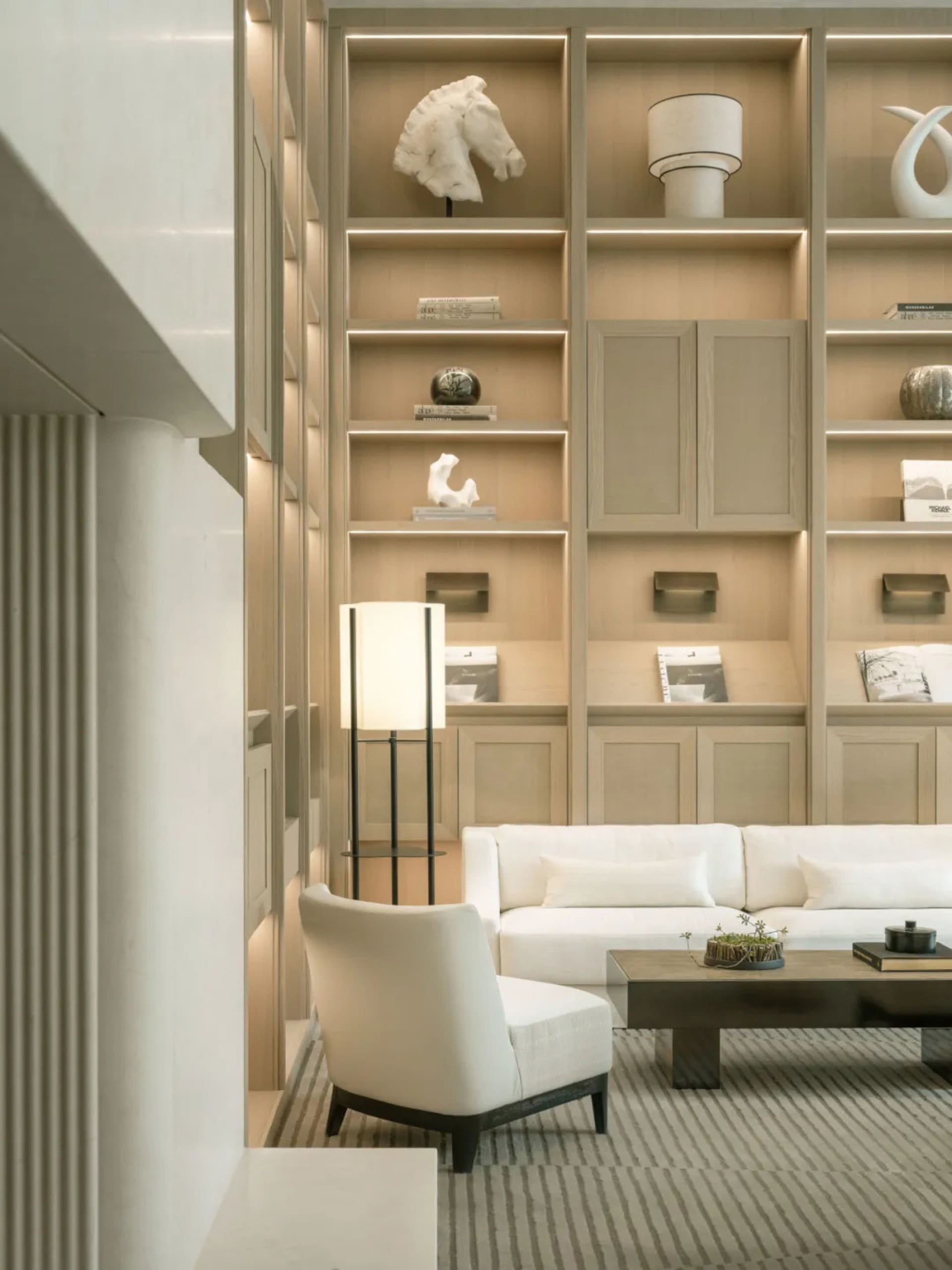 Comfortable living space with a white couch, chair, and wooden floor, filled with books and vases, and well-lit for a modern and inviting atmosphere