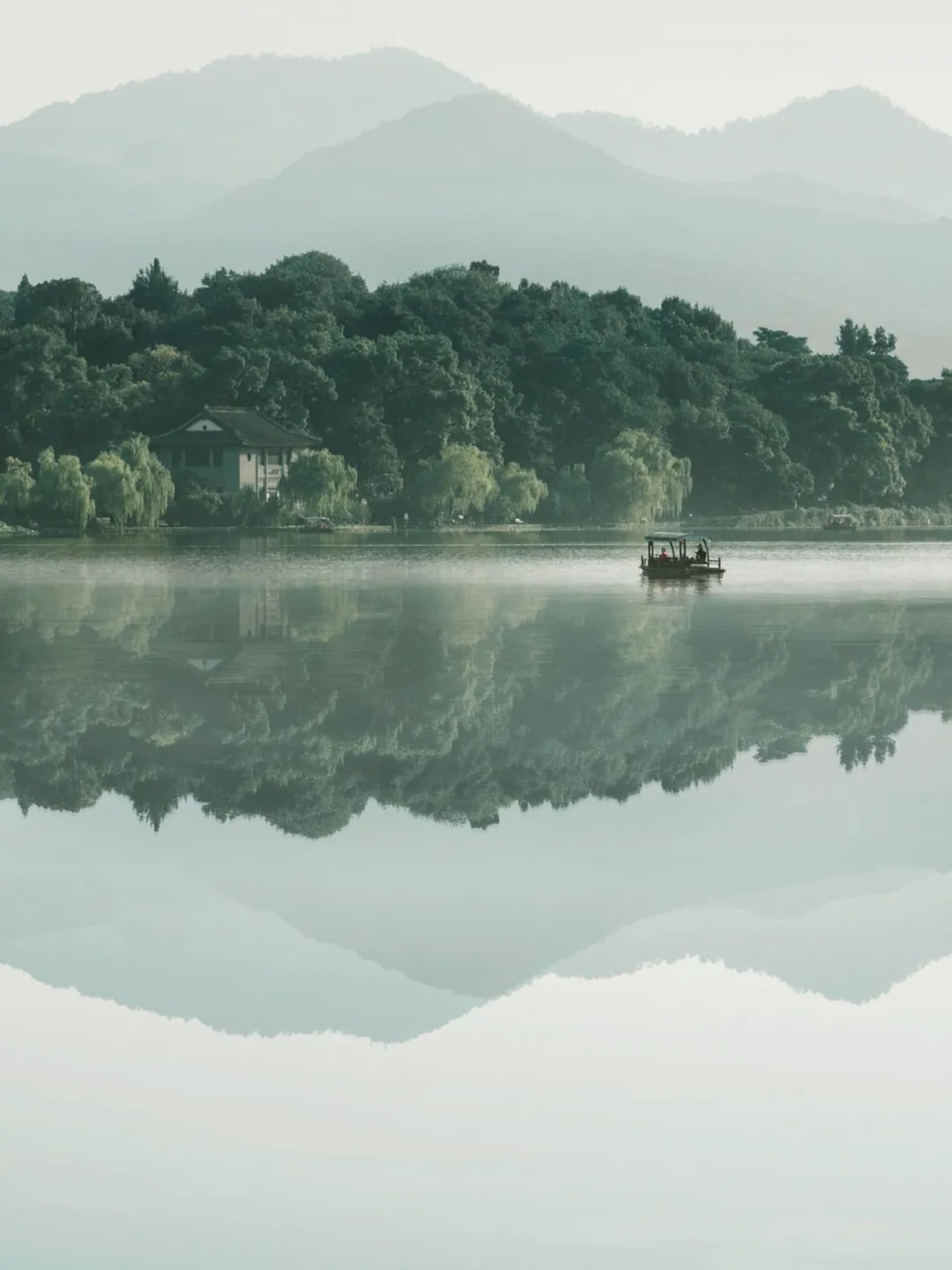A serene lakefront house with a boat floating in the water, surrounded by trees