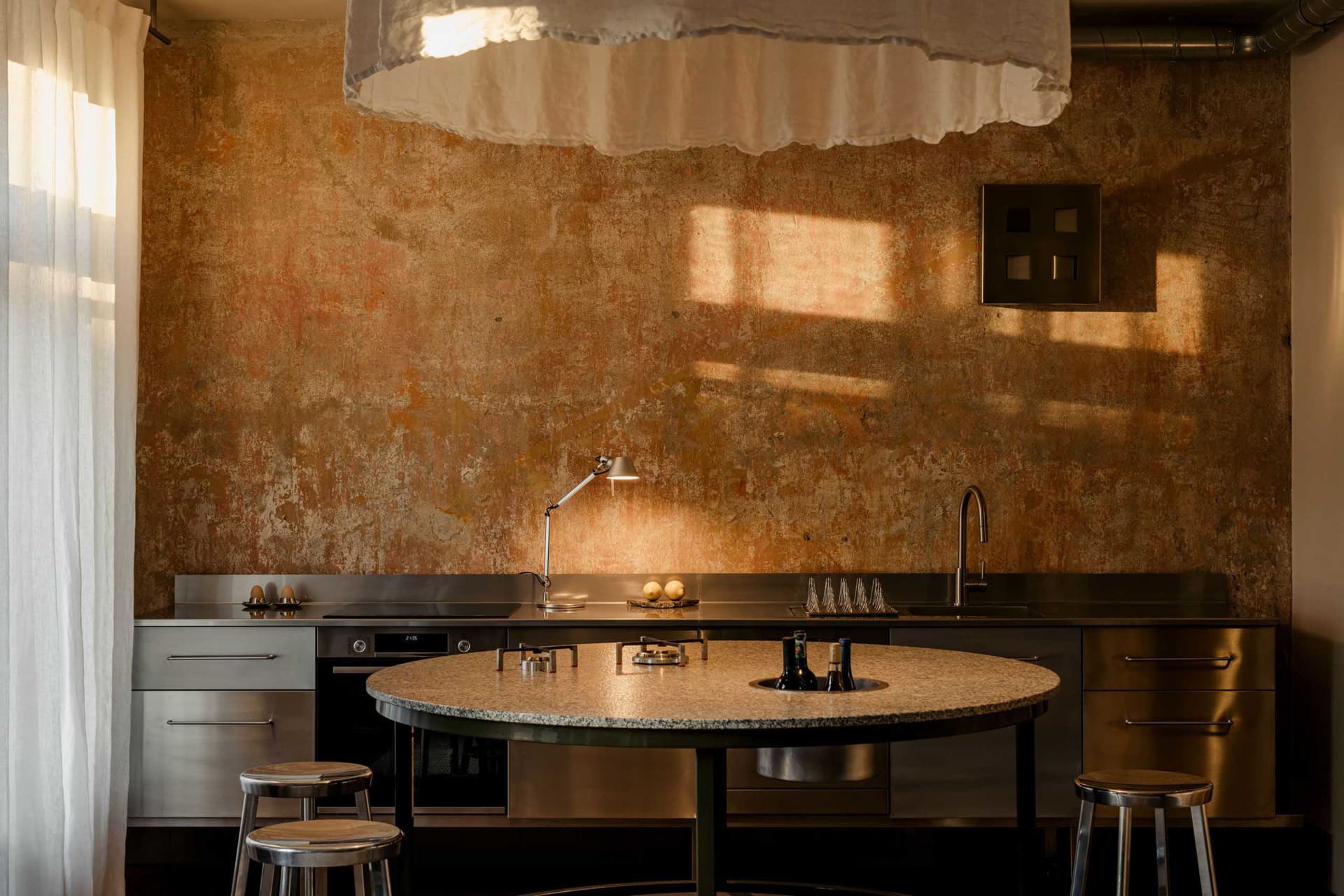 A modern kitchen with a round marble table and stools, sink, and oven, lit dimly for a cozy atmosphere