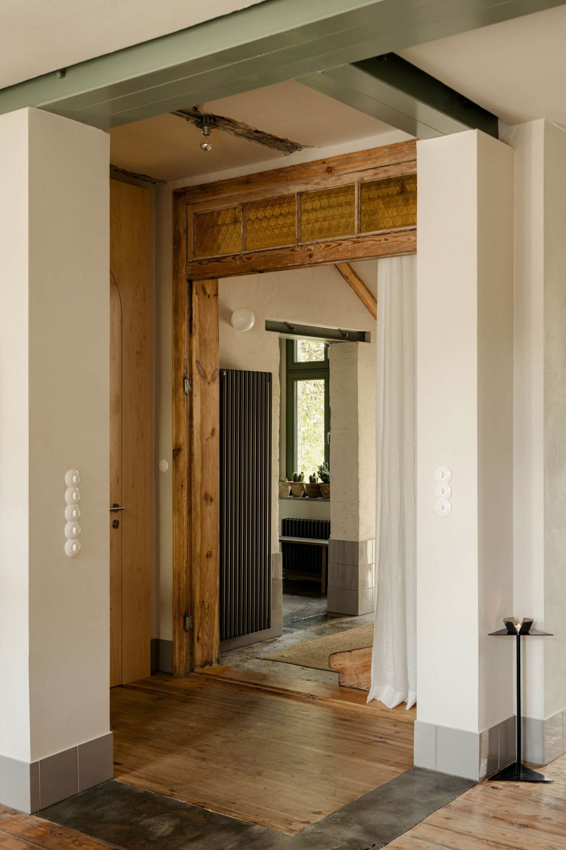 A modern kitchen with a wooden floor, a white door, and natural light from the open doorway