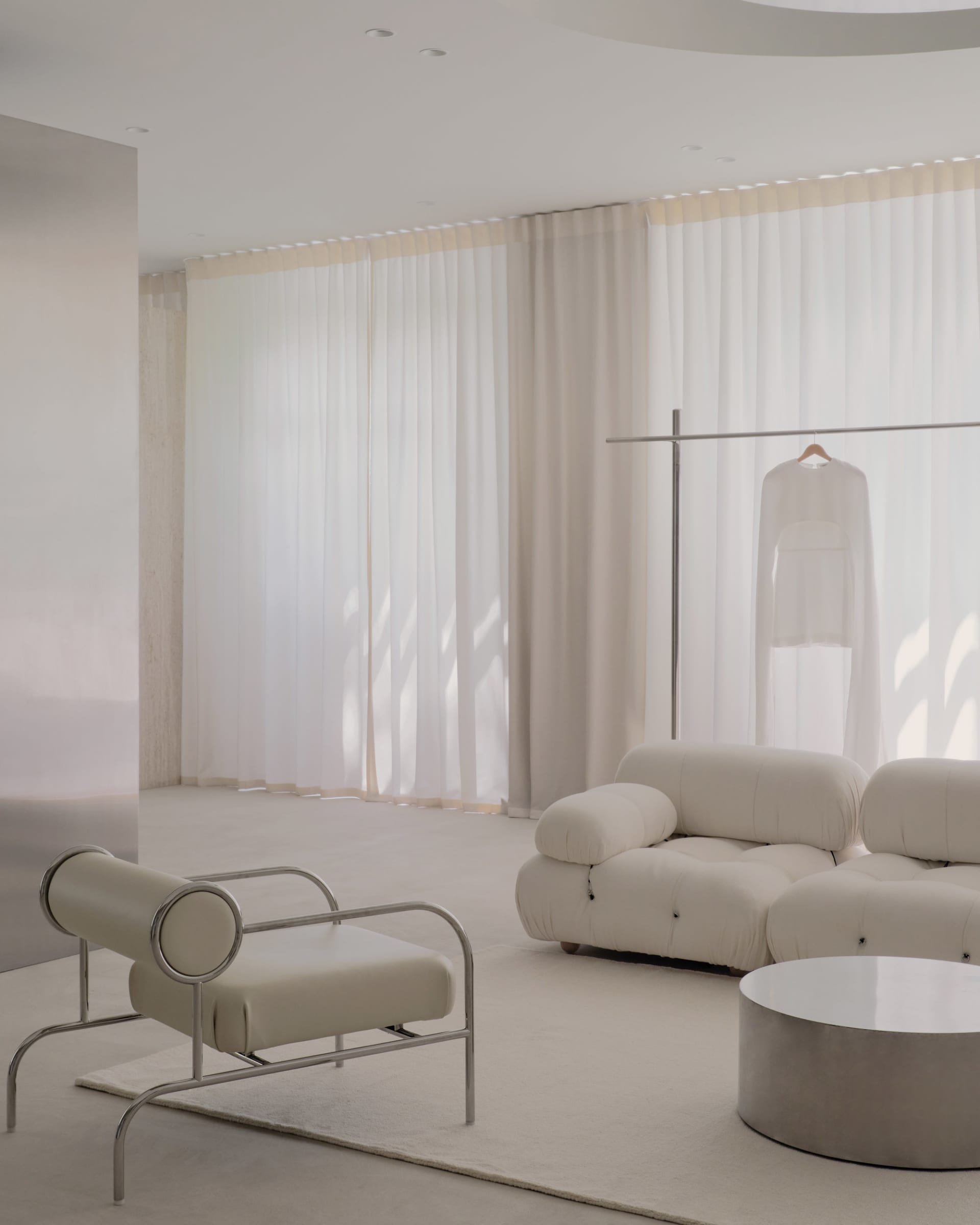 A well-lit living room with white furniture, natural light, and personal touches, featuring a couch, chair, and dining table