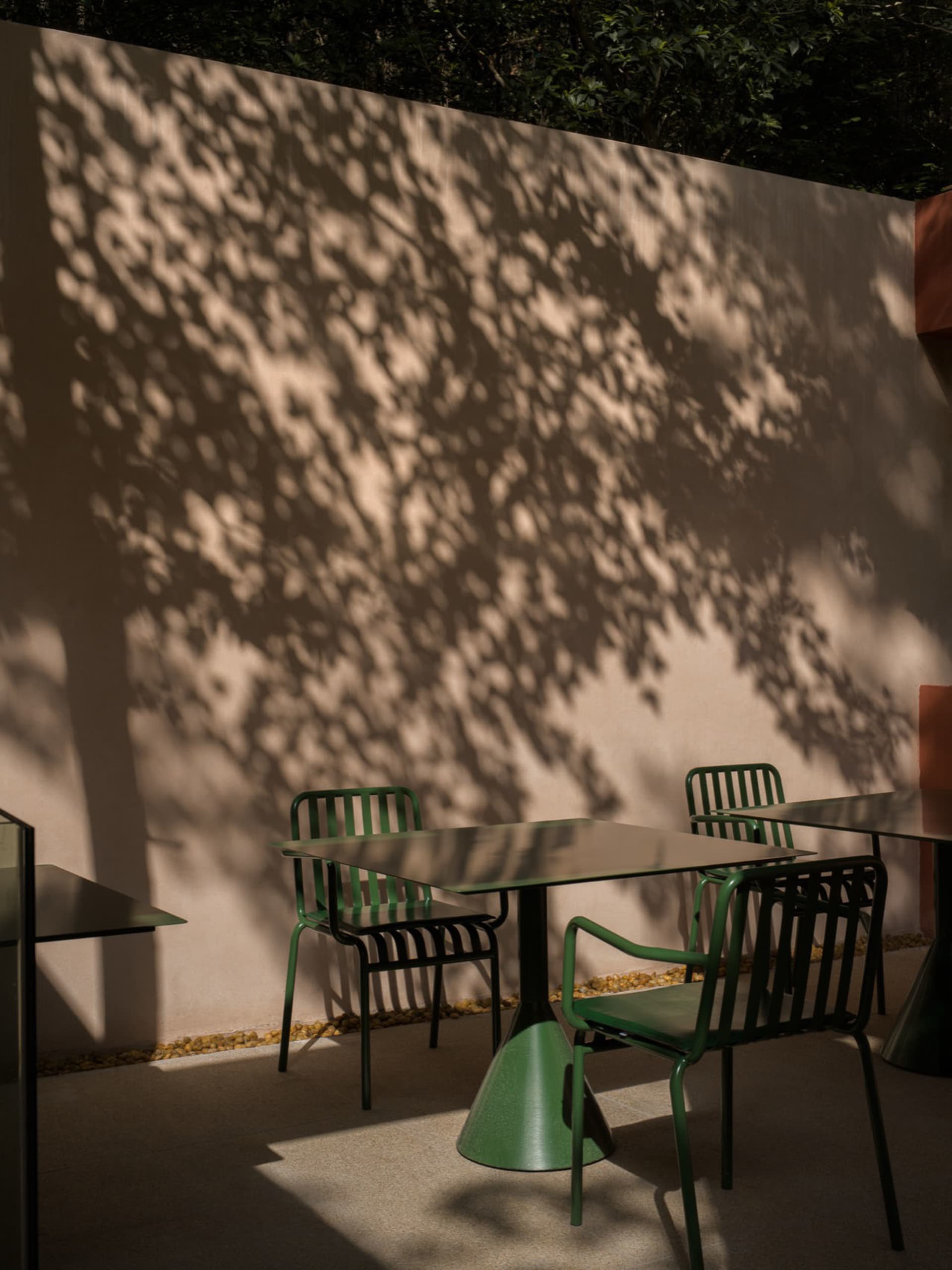 A restaurant with a patio area featuring a table and chairs surrounded by a concrete wall, with a dining table in the background, set in a warm and inviting atmosphere with natural sunlight