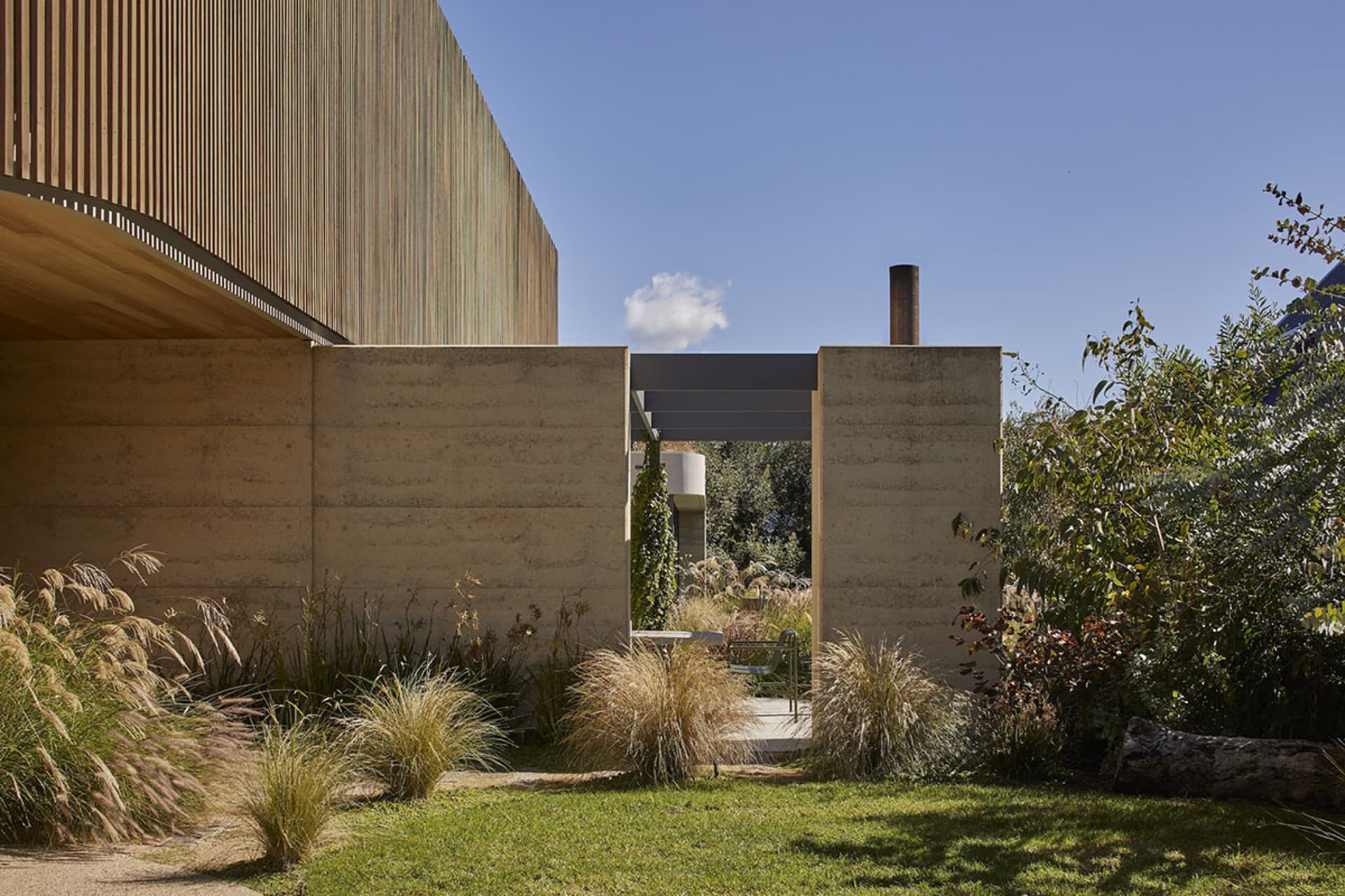 A modern house with a concrete exterior, a large window, and a patio area surrounded by greenery