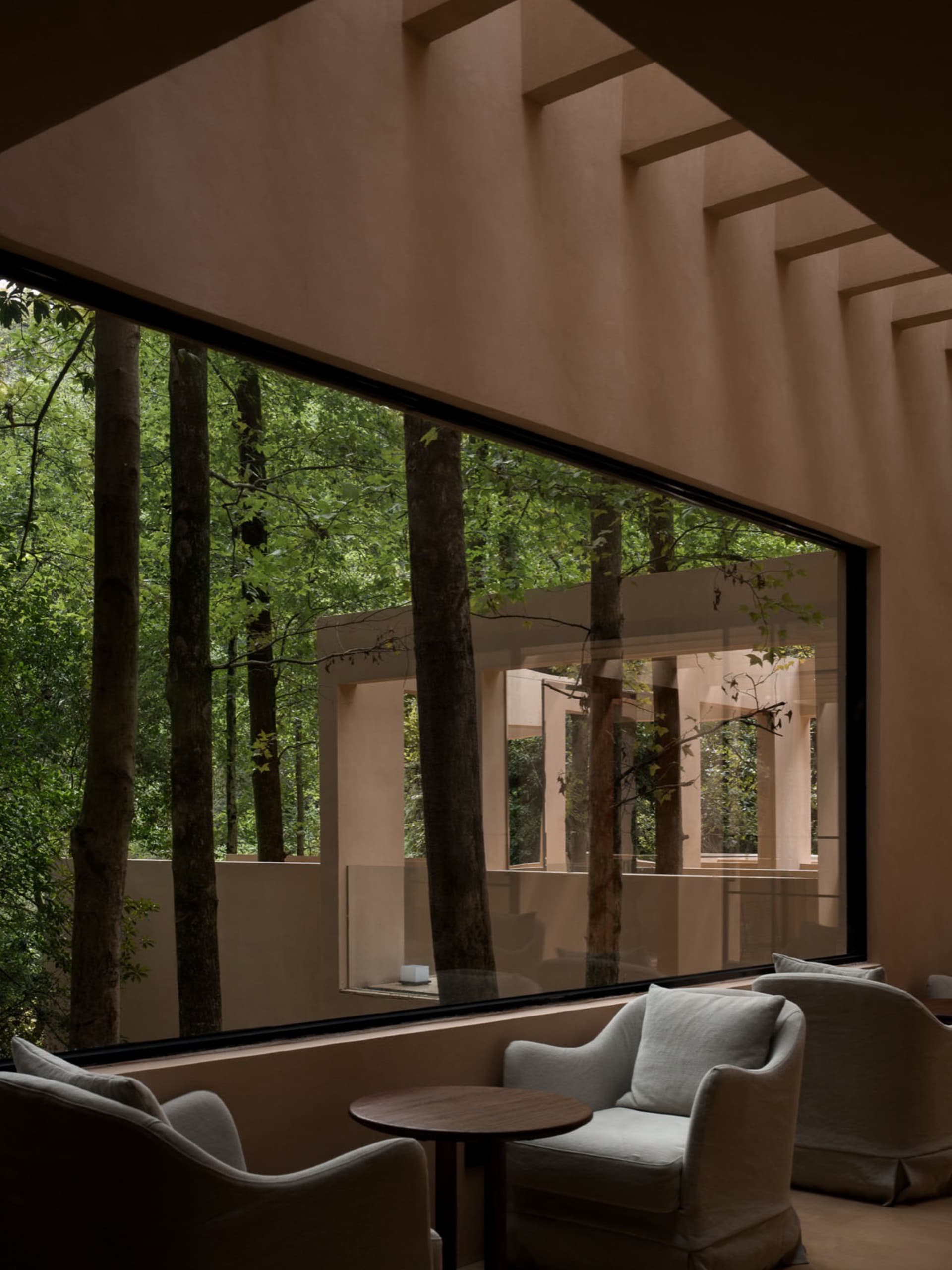 Cozy living room with a couch, chair, and dining table, surrounded by a forest view through a large window