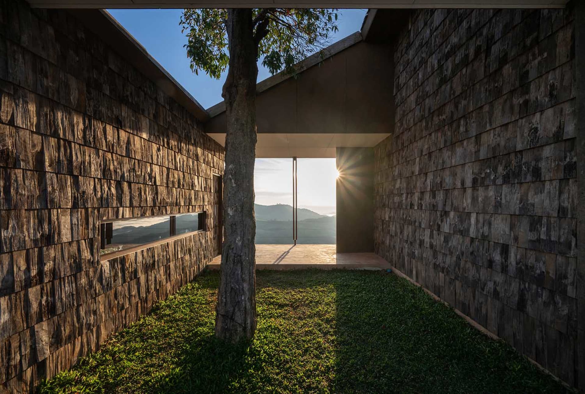 A residential house with a stone exterior and a wooden door, surrounded by a tree and natural sunlight