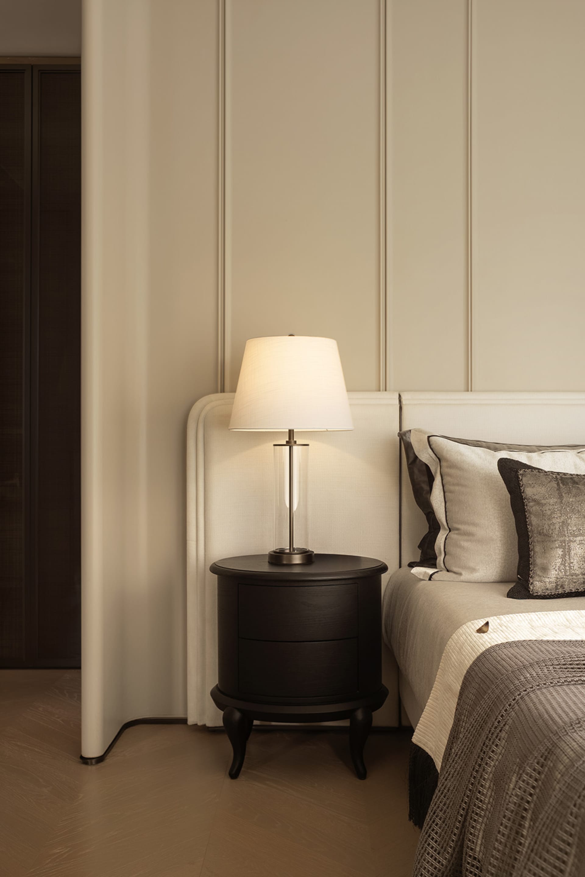A white bedroom with a bed, nightstand, and lamp, featuring a clean and bright appearance with natural light and a minimalist aesthetic