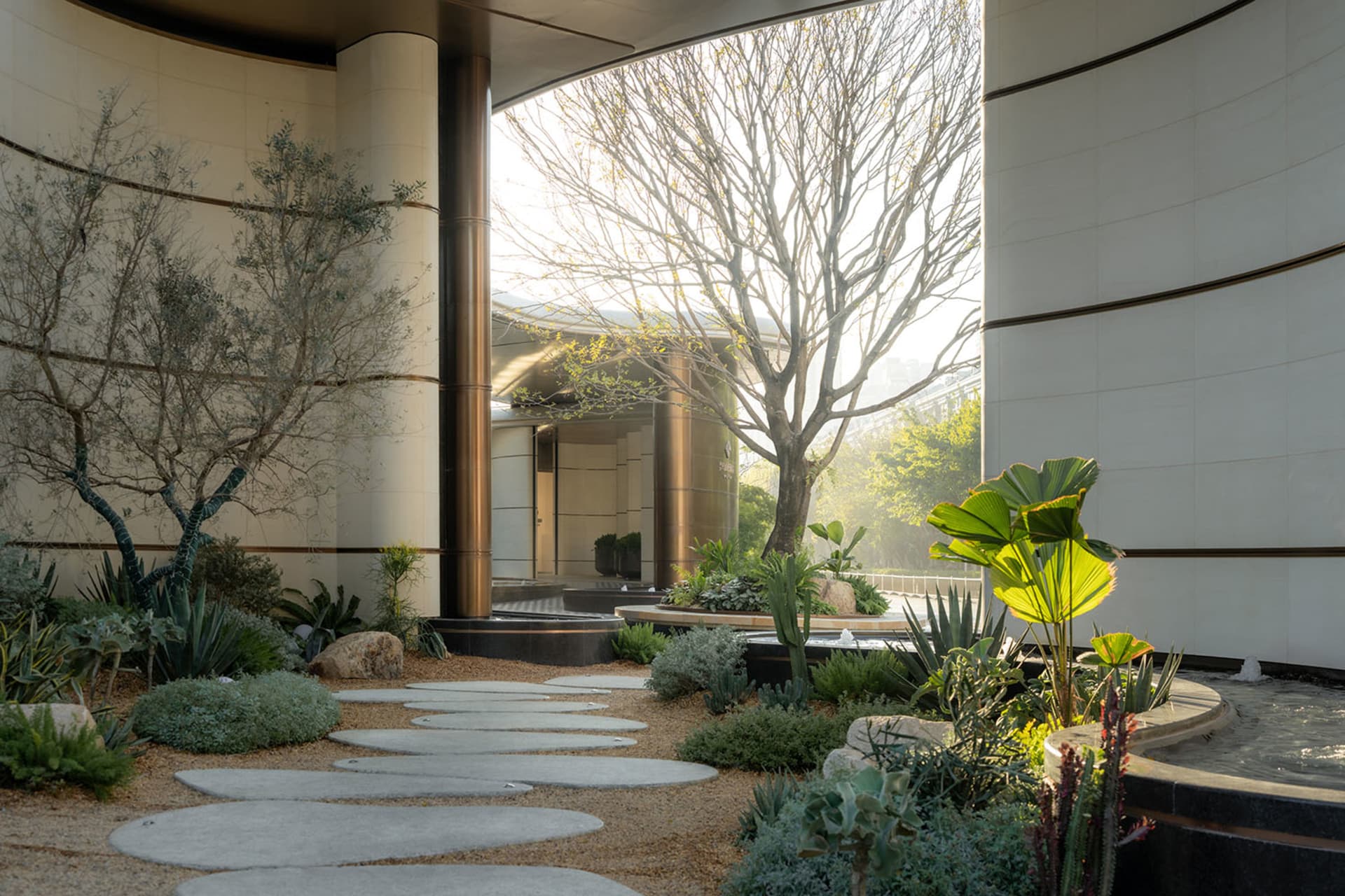 A modern building with a large garden featuring a tree, surrounded by lush greenery and natural light