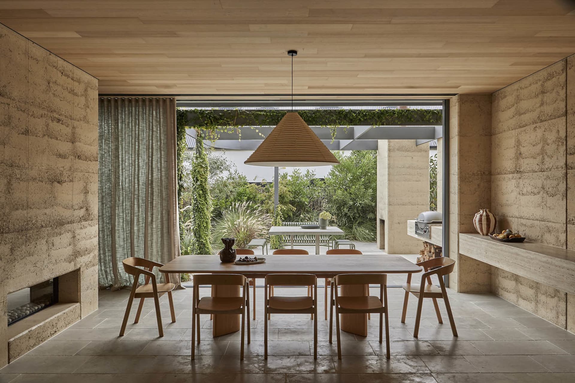 A modern dining room with a wooden table and chairs, surrounded by a large window and a kitchen in the background, with a clean and minimalist design
