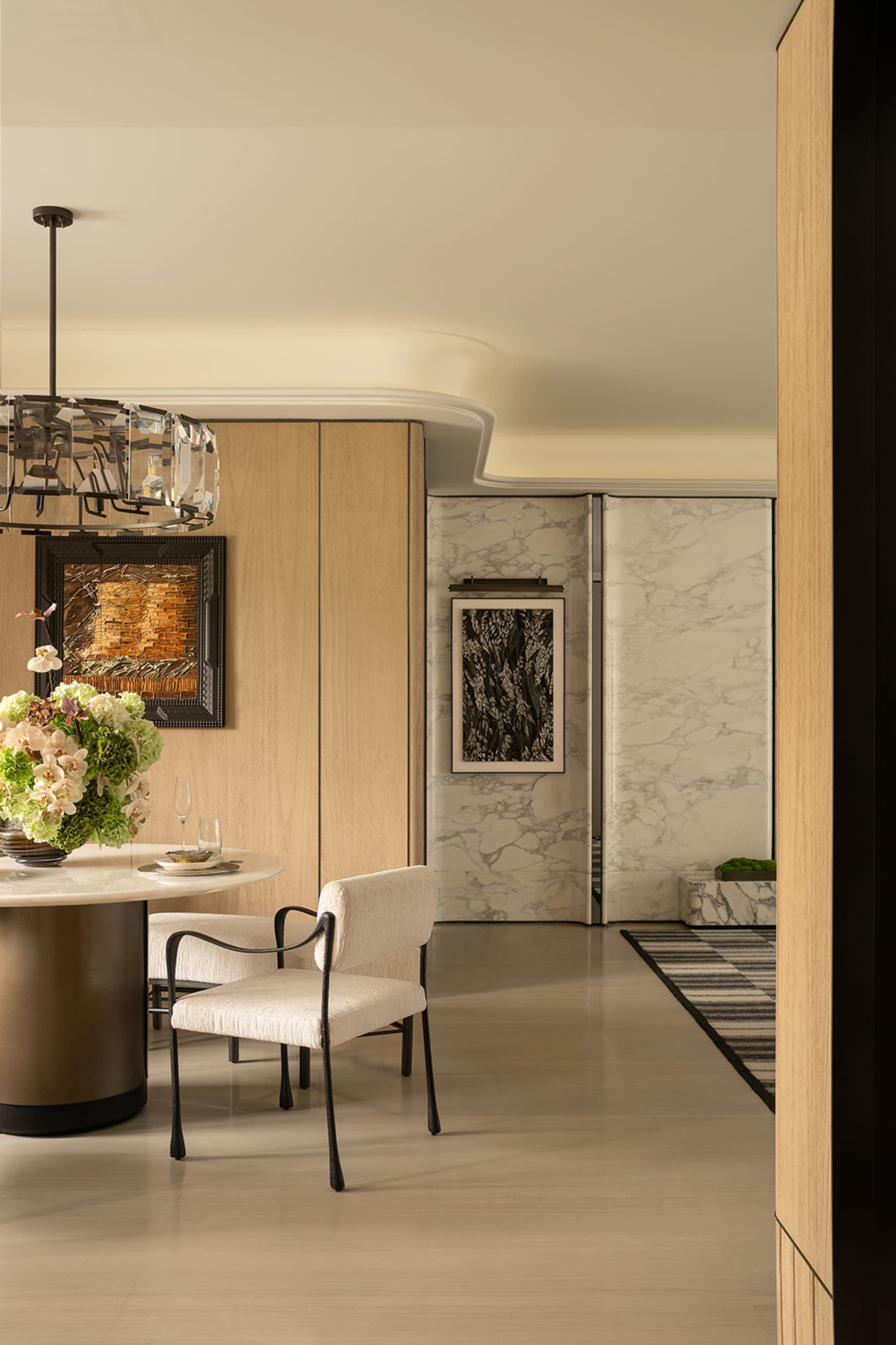 Modern dining room with a chandelier, dining table, chairs, and a potted plant, set for a meal or gathering