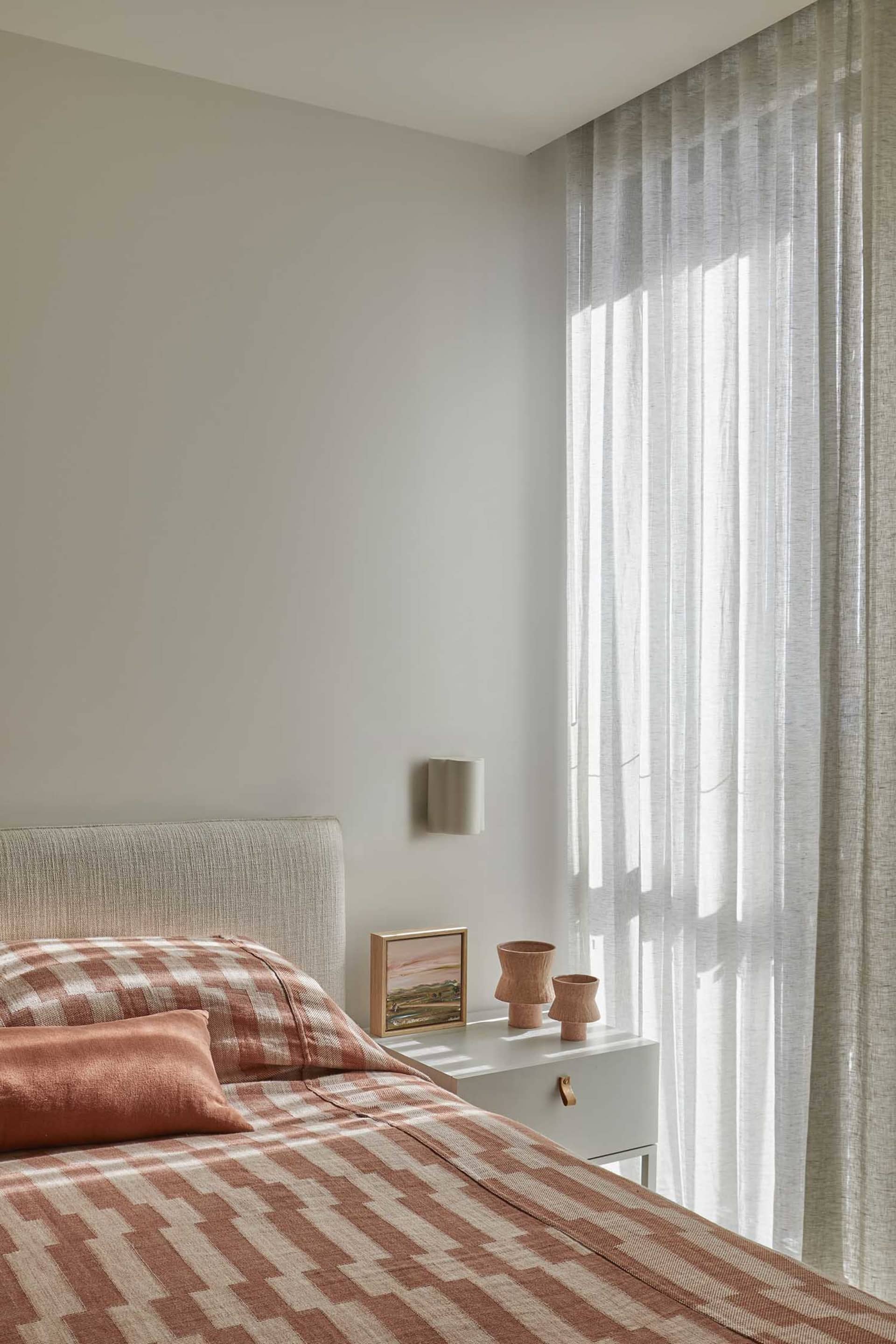 Cozy bedroom with a bed, dresser, and natural light from a window, featuring a white color scheme and plaid blanket