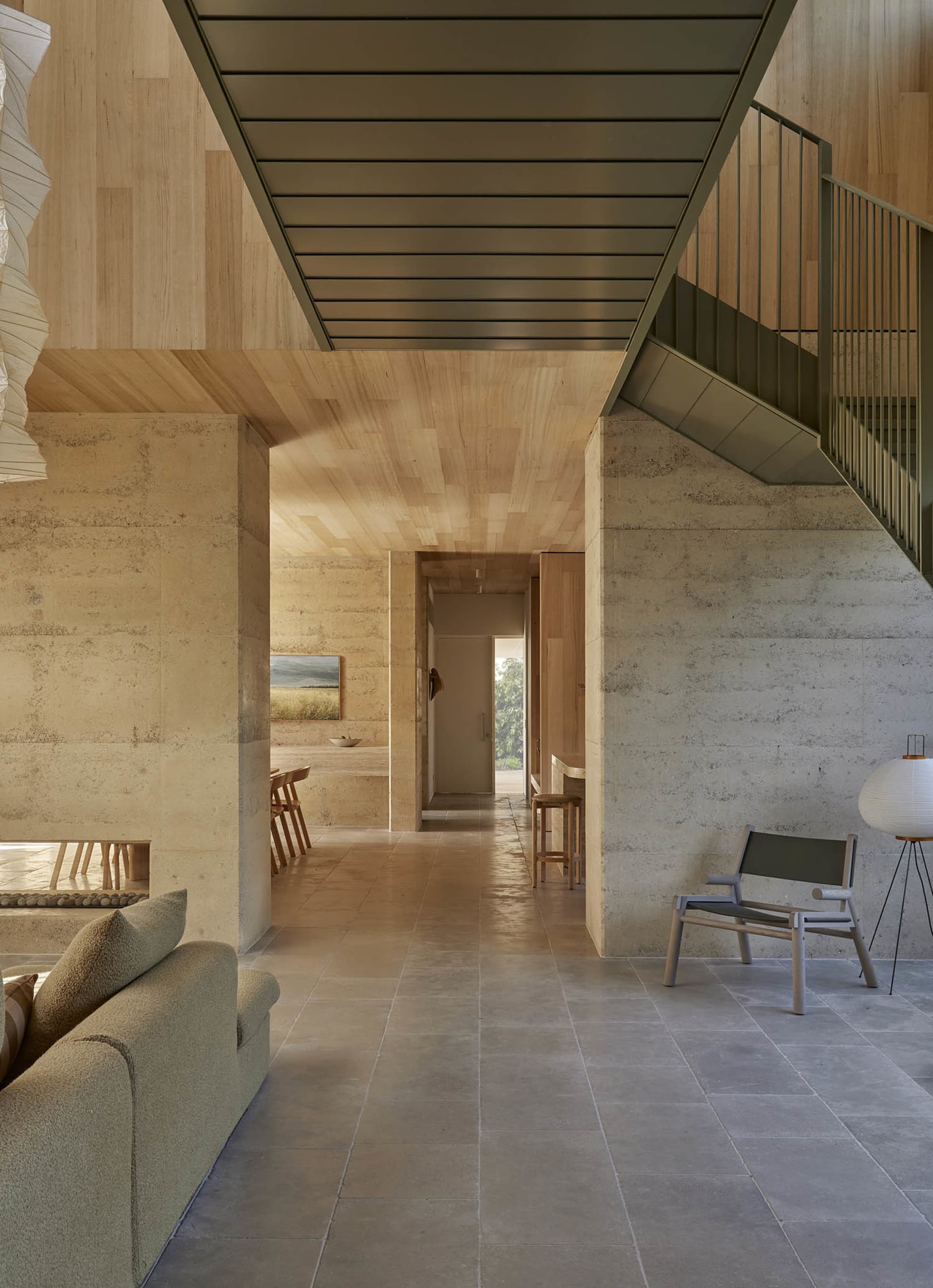 Cozy living room with a couch, chair, and dining table on a wooden floor, near a staircase, with natural light from windows