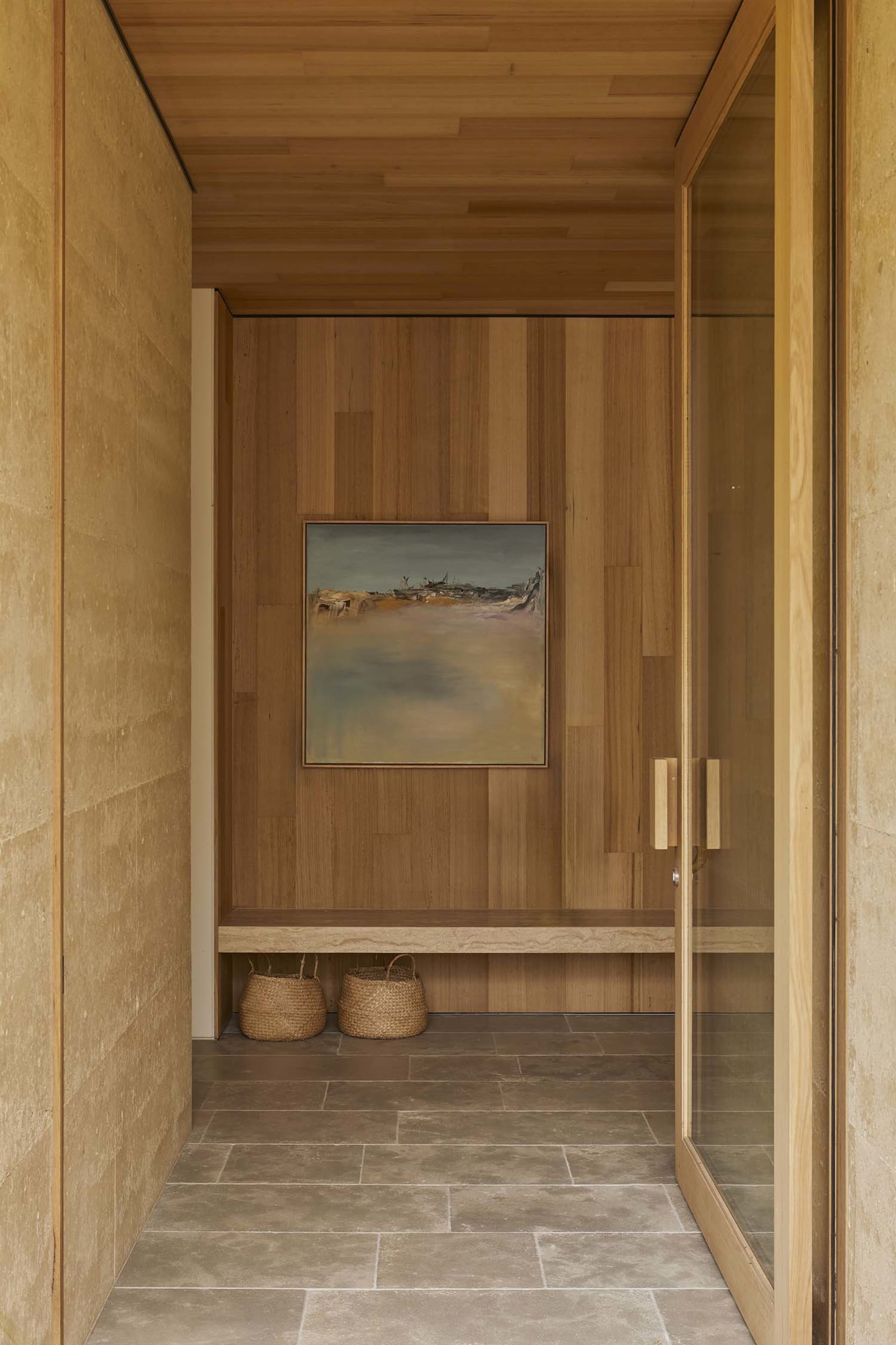 A modern bathroom with a wooden door and a beach scene painting on the wall, featuring a bench and a doorway, with dim lighting creating a cozy atmosphere
