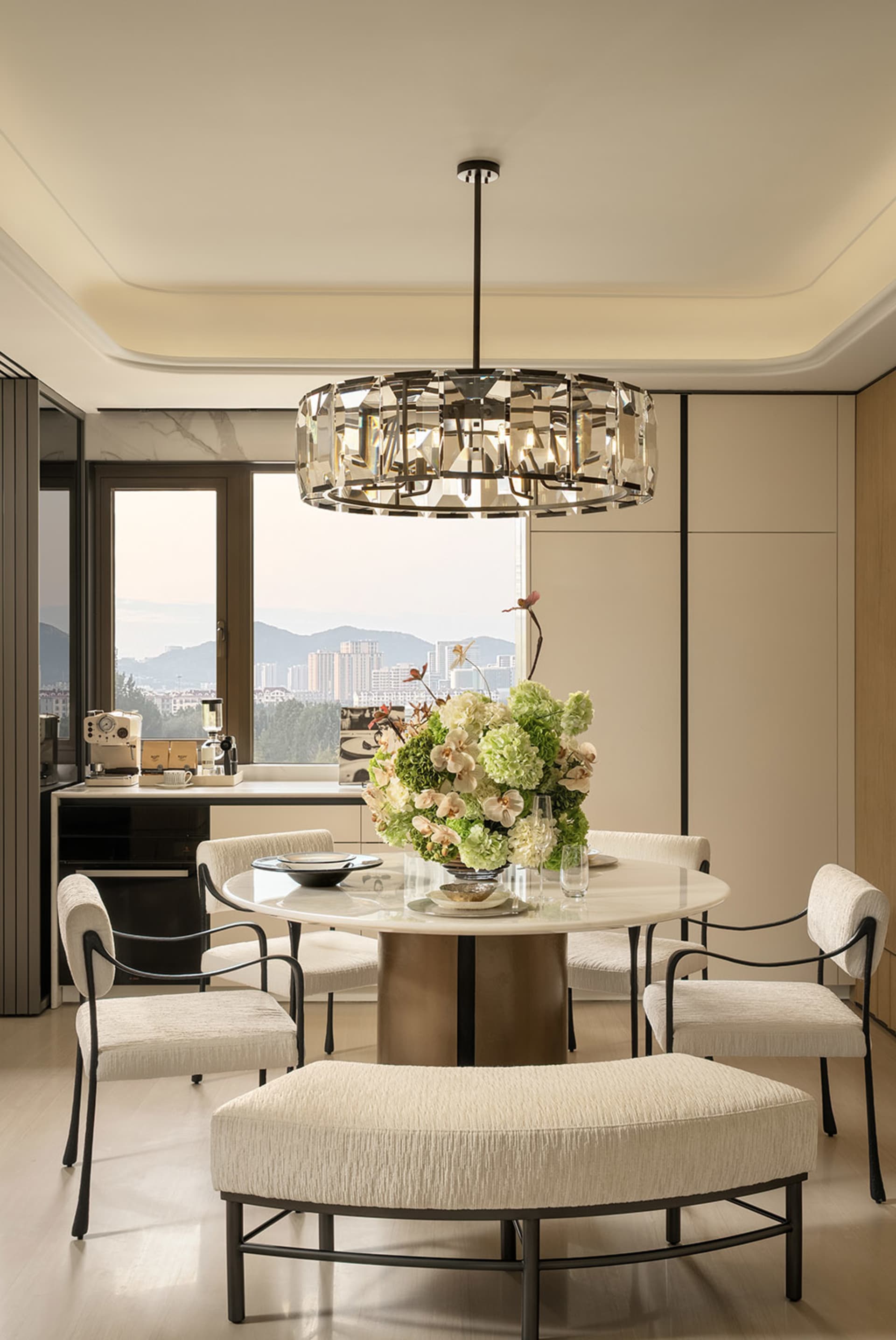 Dining room with a round table surrounded by chairs, a vase with flowers, and a modern style, with natural lighting creating a warm and inviting atmosphere