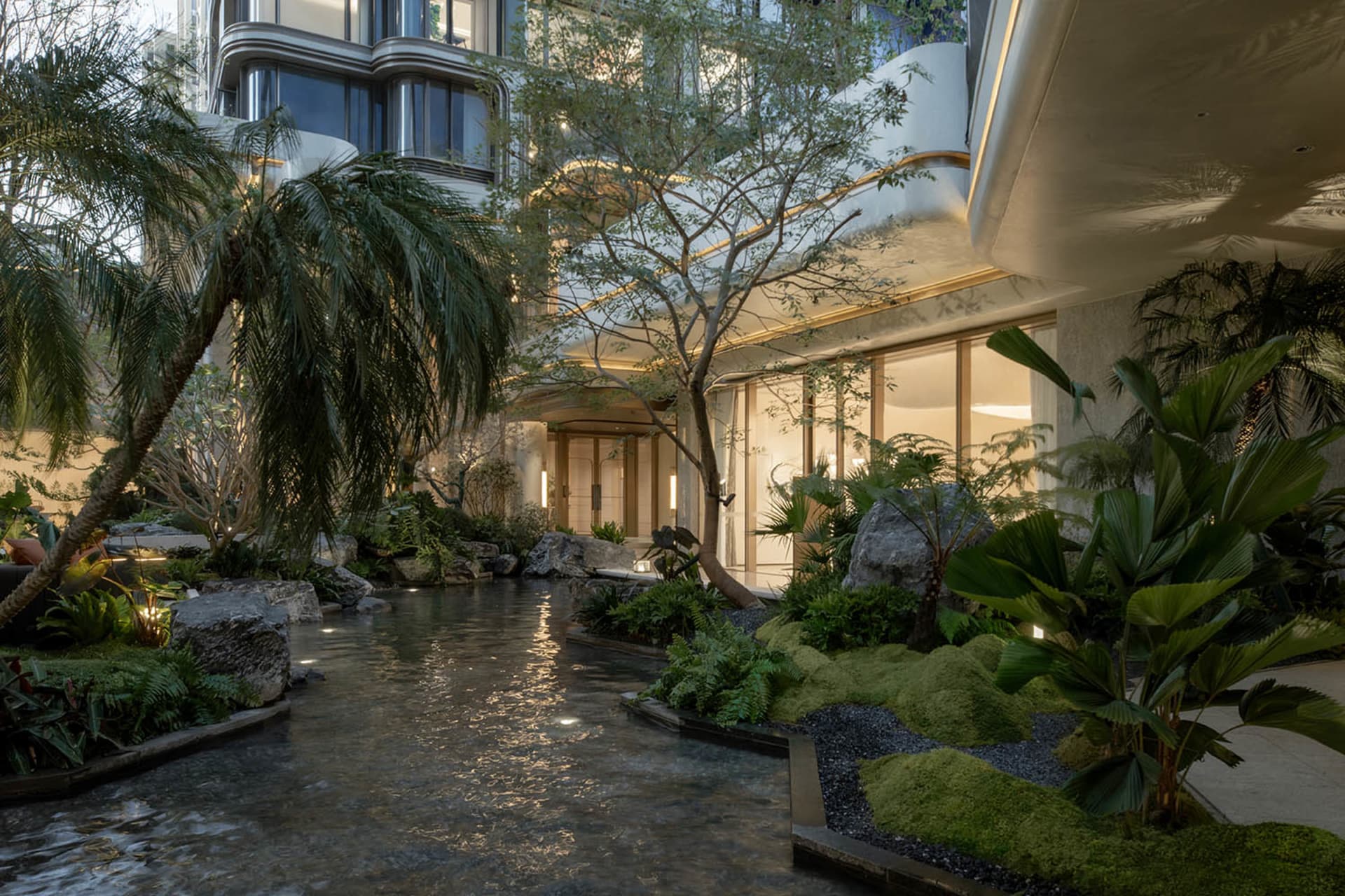 A serene and calming atrium with a waterfall, featuring a mix of glass and concrete elements, surrounded by a large building with soft and diffused lighting