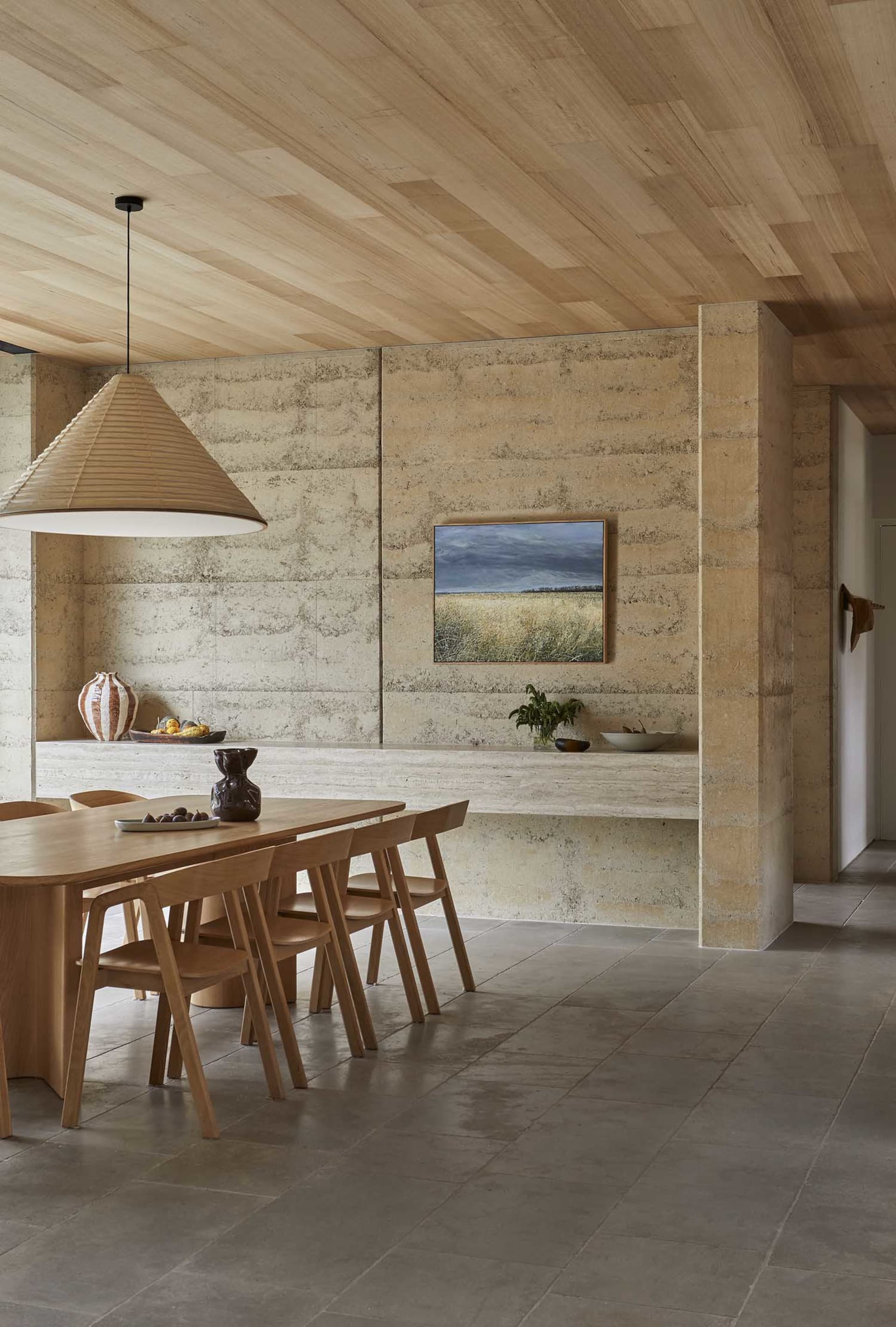 A modern kitchen with a dining table and chairs, surrounded by a counter with a vase, featuring wood and stone materials in a well-lit space