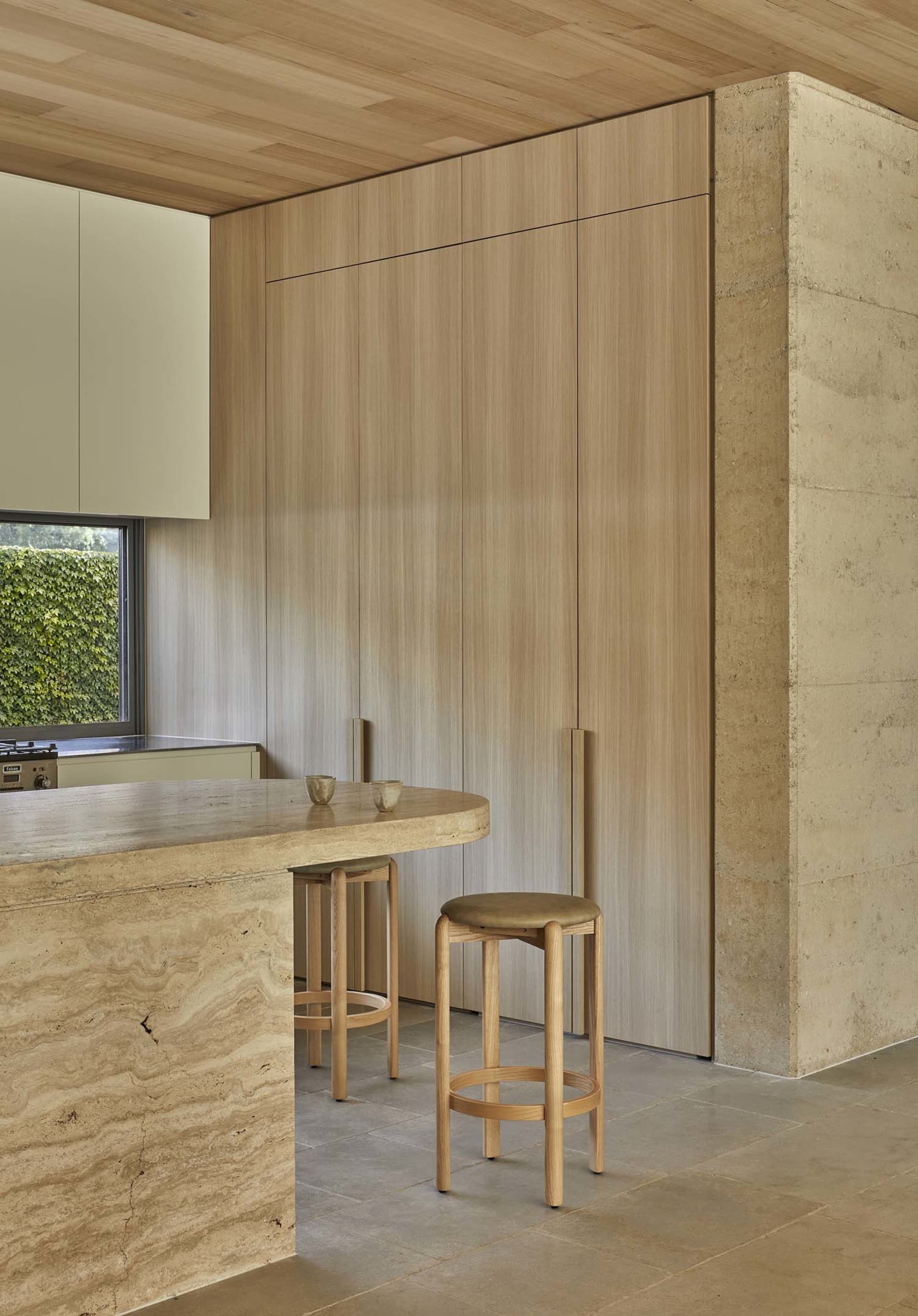 A modern kitchen with wooden cabinets, a marble countertop, and a dining table with chairs, featuring soft and warm lighting