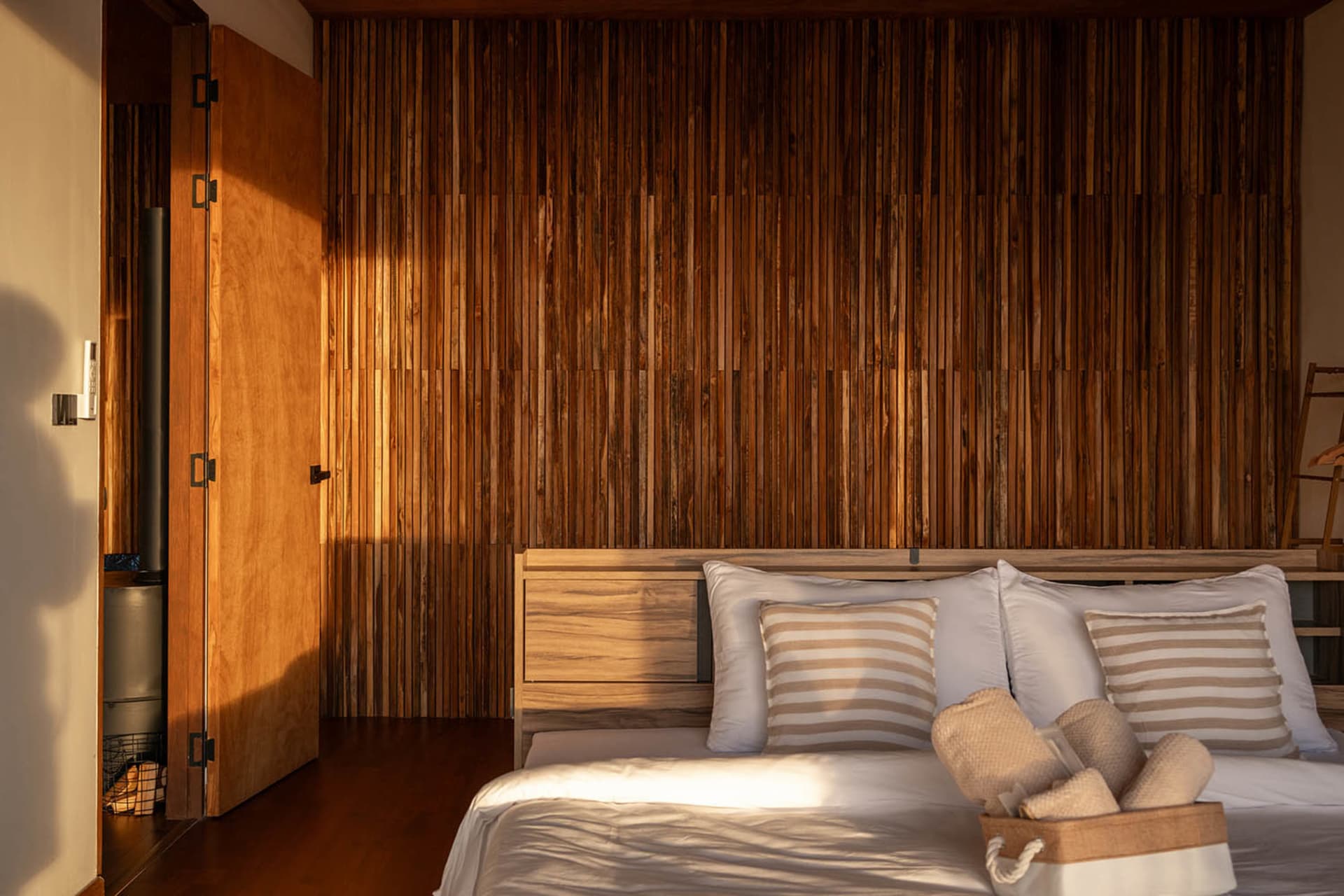 Dimly lit bedroom with a wooden wall and headboard, featuring a bed with two pillows