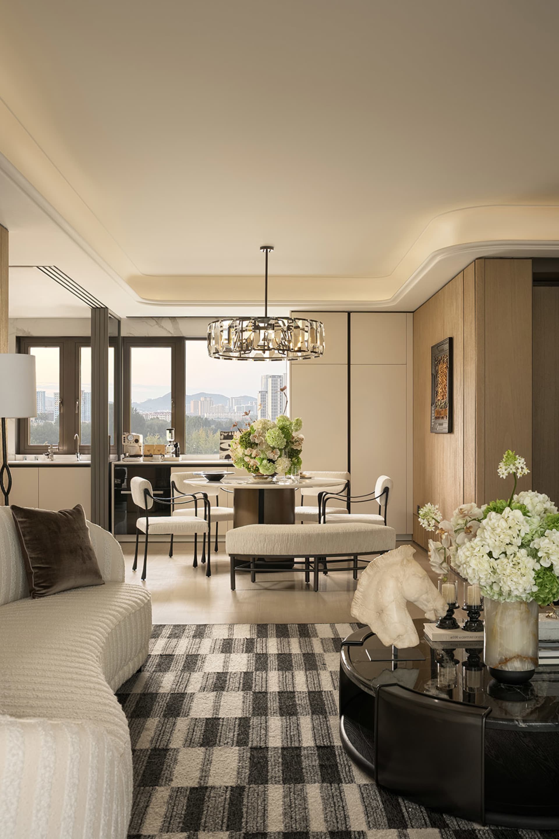 Comfortable modern living space with a large window, a couch, dining table, and chandelier, well-lit with natural light and elegant decor