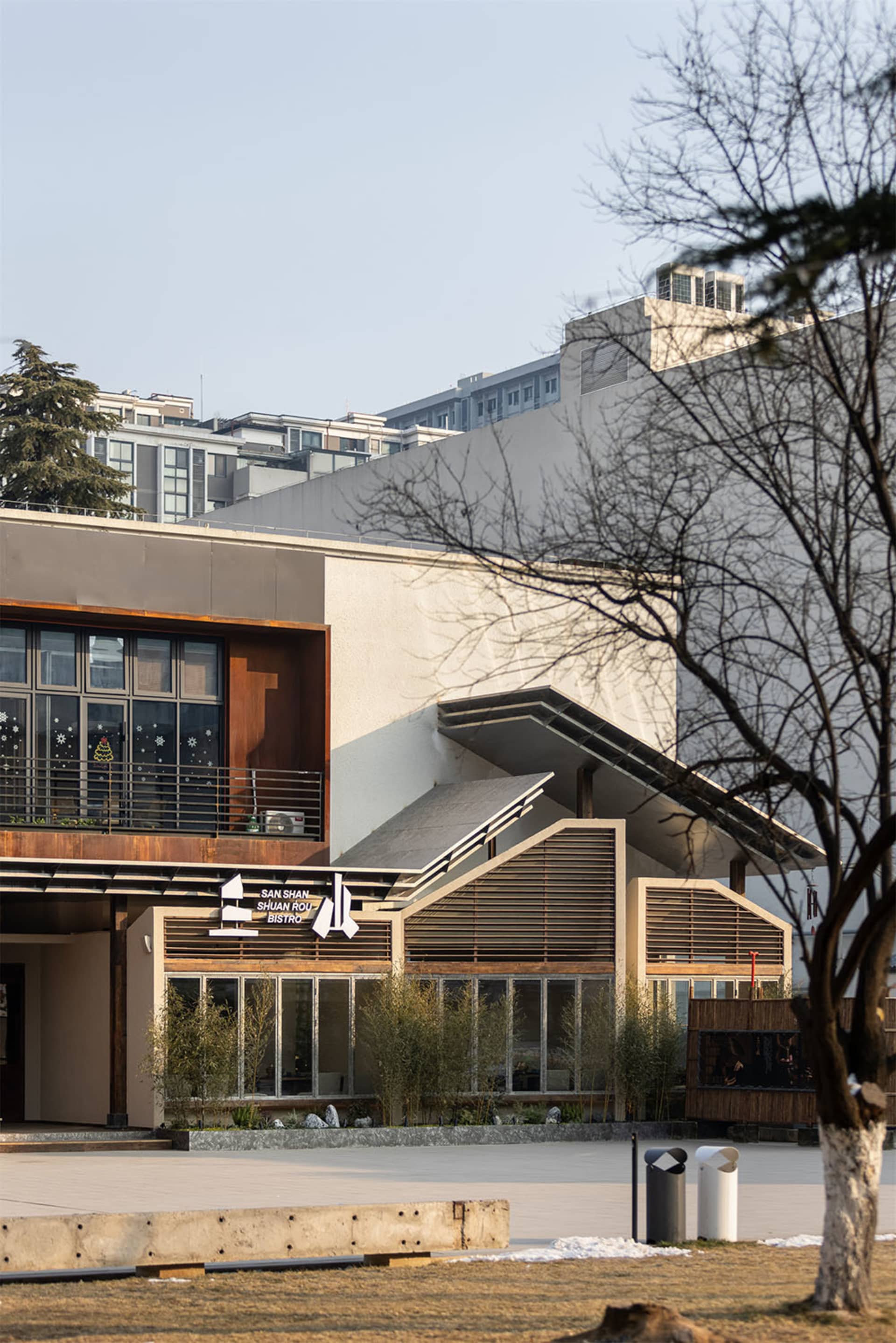 A modern building with a large white concrete wall and a tree in front, creating a calm and serene atmosphere