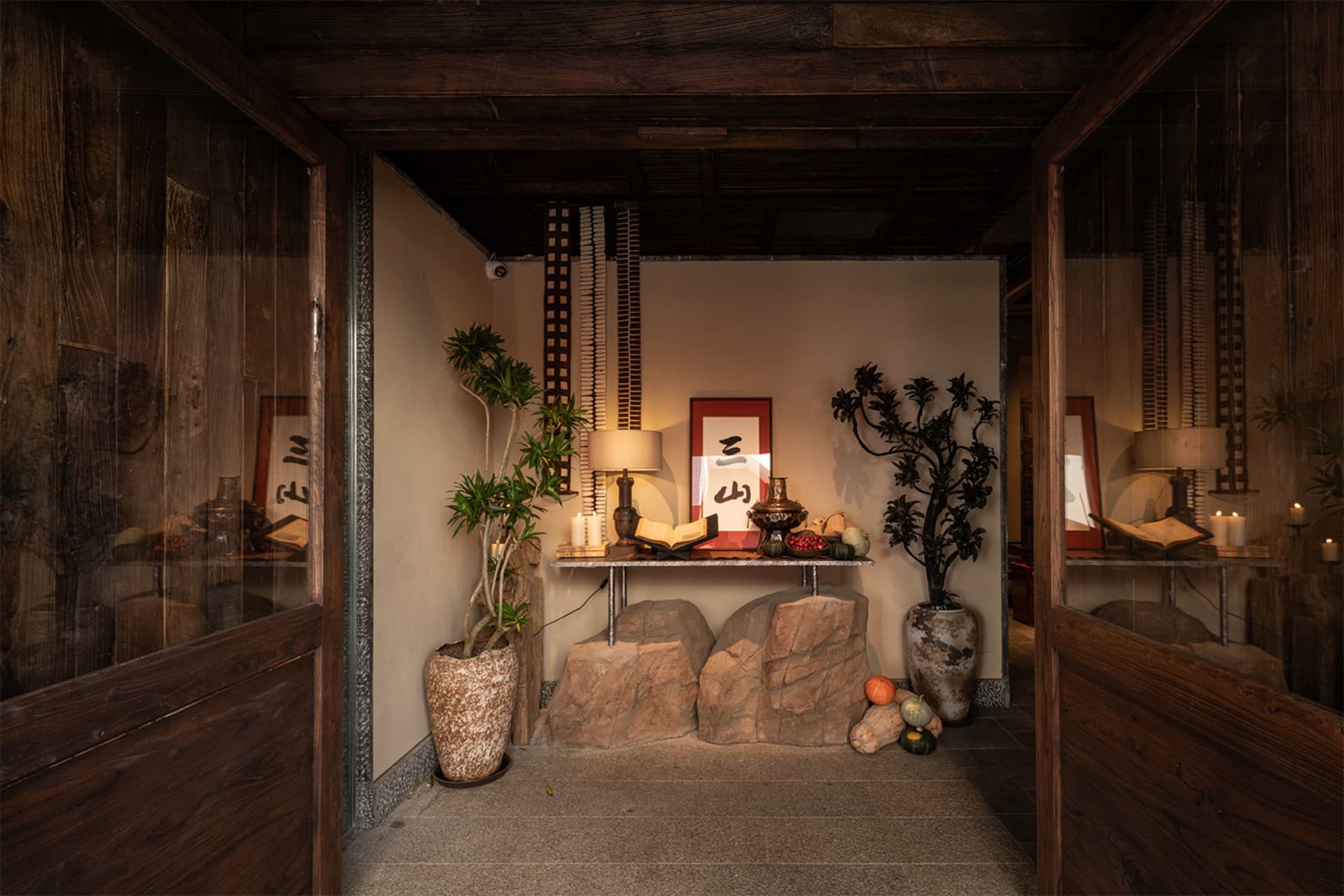 Cozy living space with a wooden floor, stone walls, a rock wall, and dim lighting, featuring a stone bench, potted plant, and decorative vases