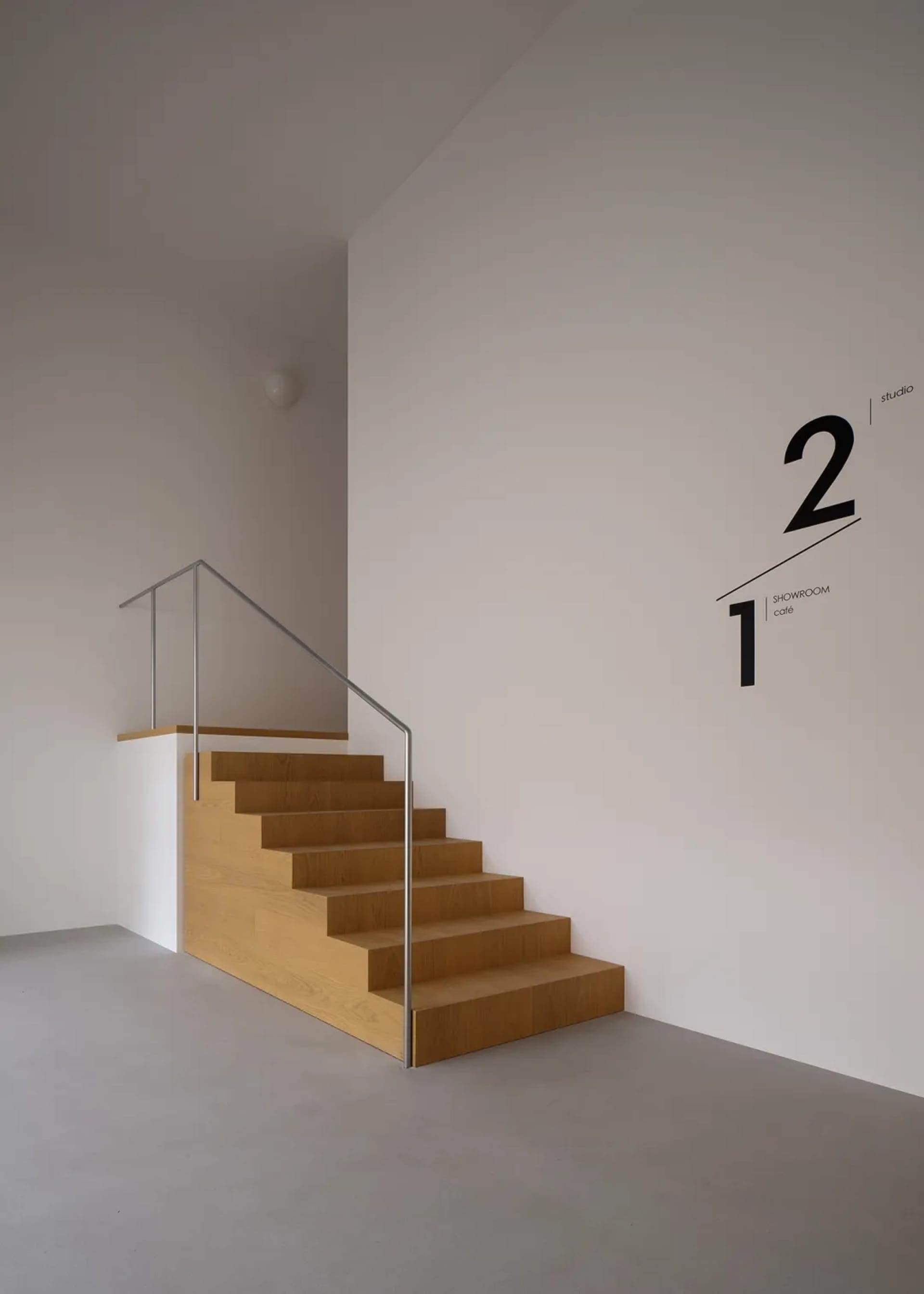 A dimly lit room with a minimalist wooden staircase and metal railing, featuring a white wall with a number 2