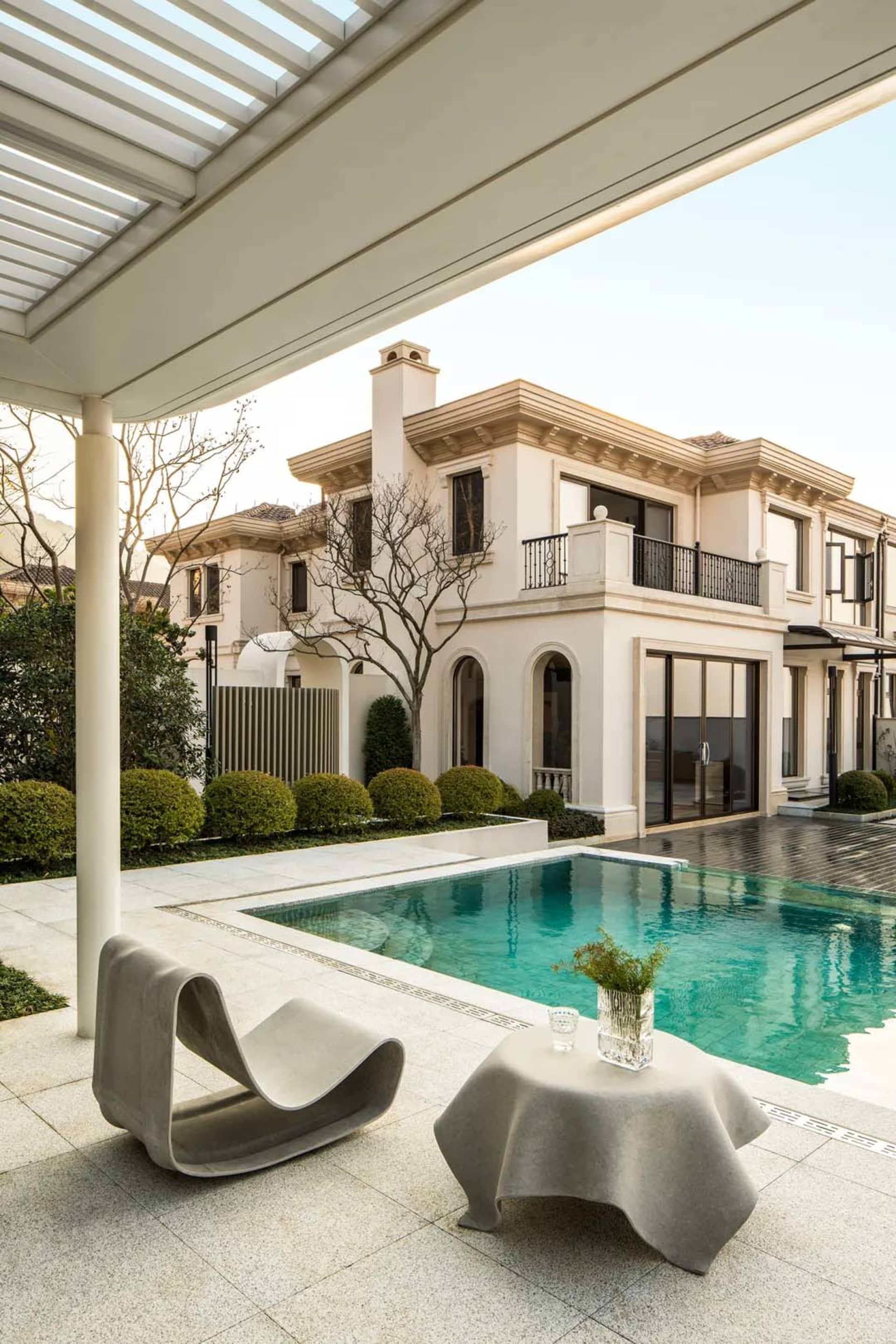 A modern house with a white facade, surrounded by a garden and featuring a large pool in the backyard, with natural lighting creating a bright and inviting ambiance