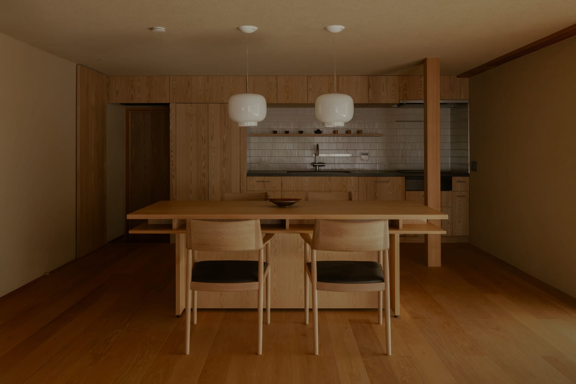 Warm and inviting kitchen with wooden floors, furniture, and a dining table, surrounded by chairs and a counter with a sink