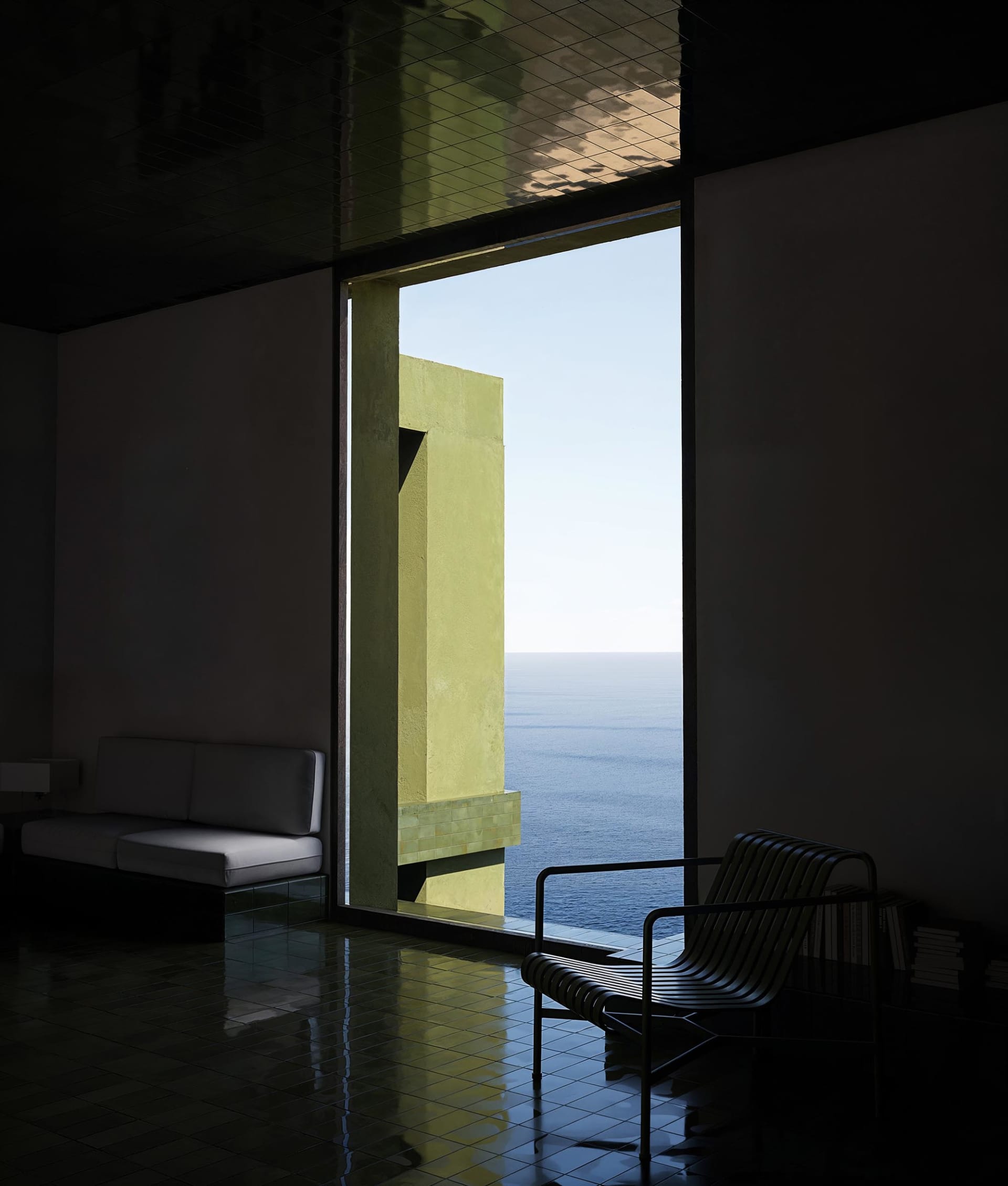 A well-lit living room with a couch and chair in front of a large ocean-facing window, featuring a mix of wood and metal furniture and decor