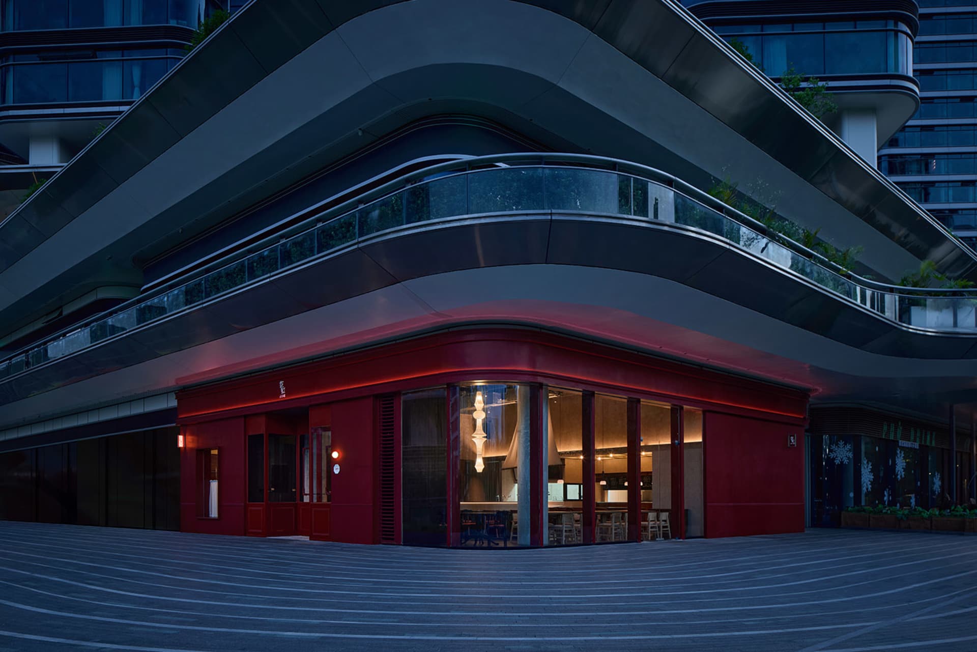 A modern restaurant with a red brick facade, featuring a large window and a cozy interior with chairs and dining tables