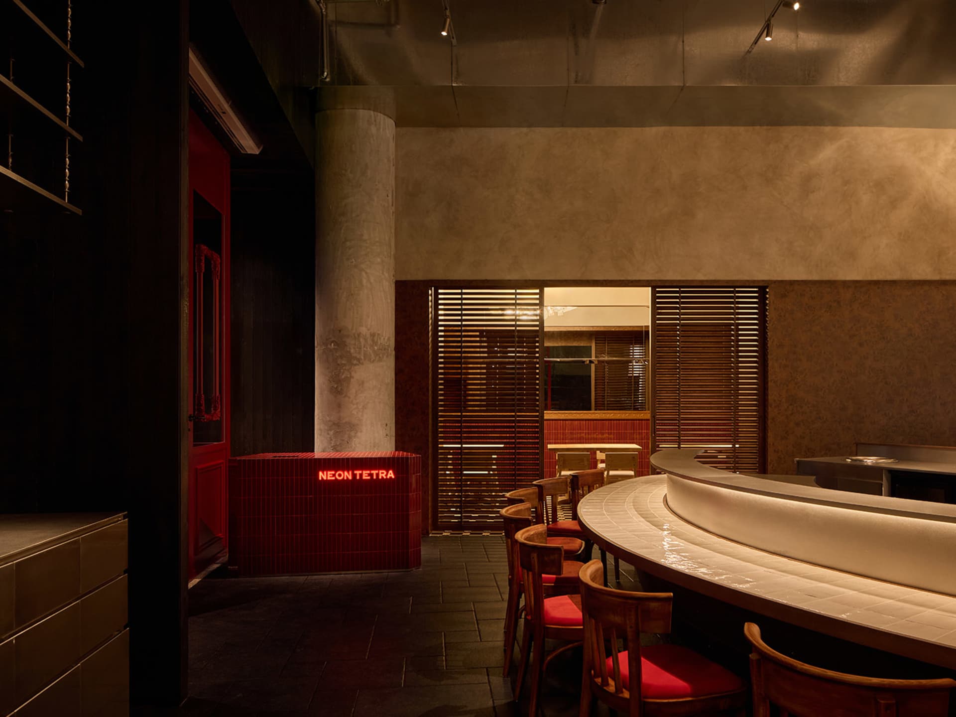 Cozy restaurant interior with a wooden bar, red chairs, and dim lighting, featuring a mix of wood and metal elements