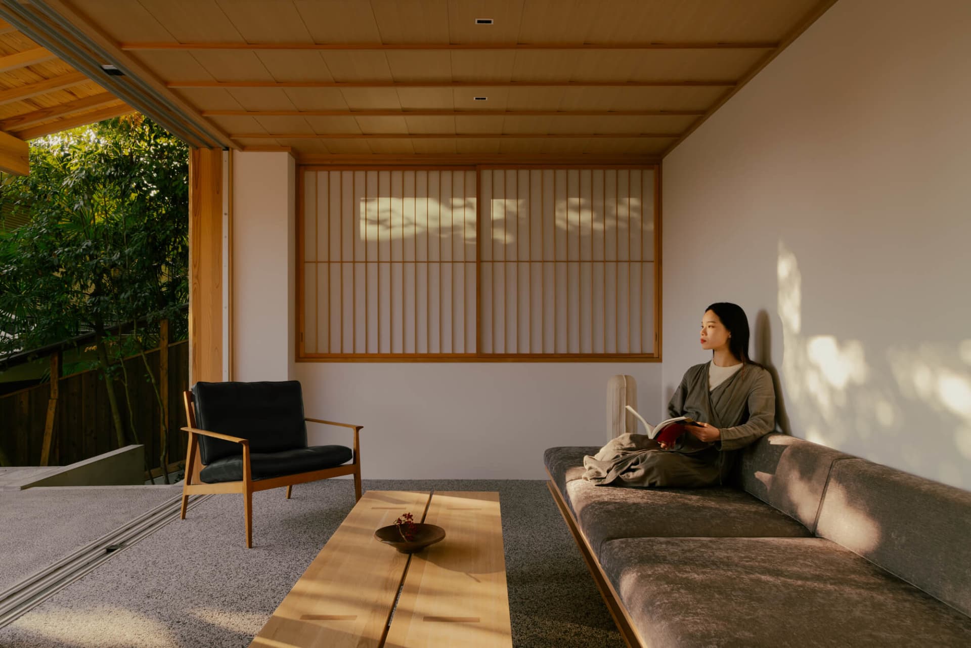 A well-lit living room with a woman reading on a couch, surrounded by wooden furniture and a warm atmosphere