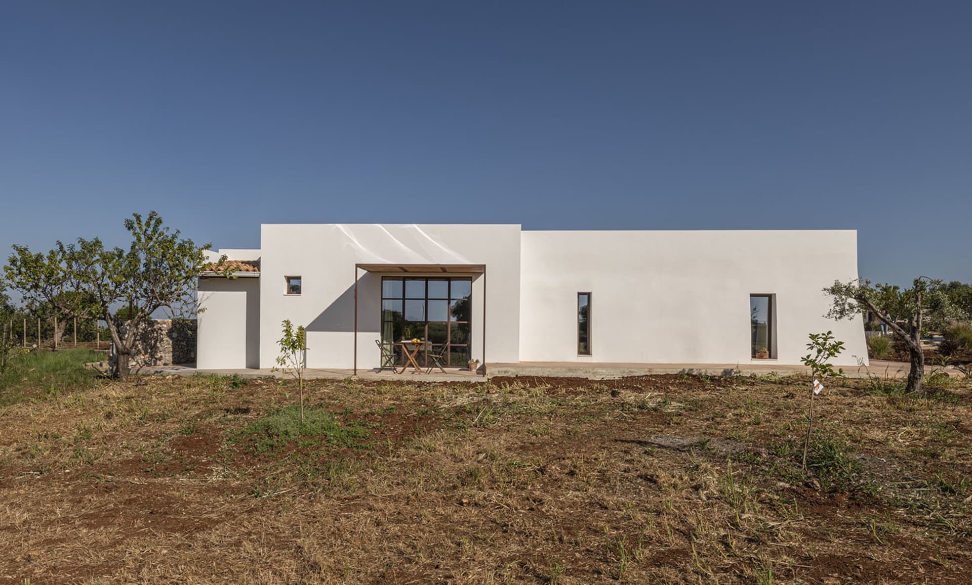 A modern house with a white exterior, surrounded by a grassy area, with a large patio and architectural details visible