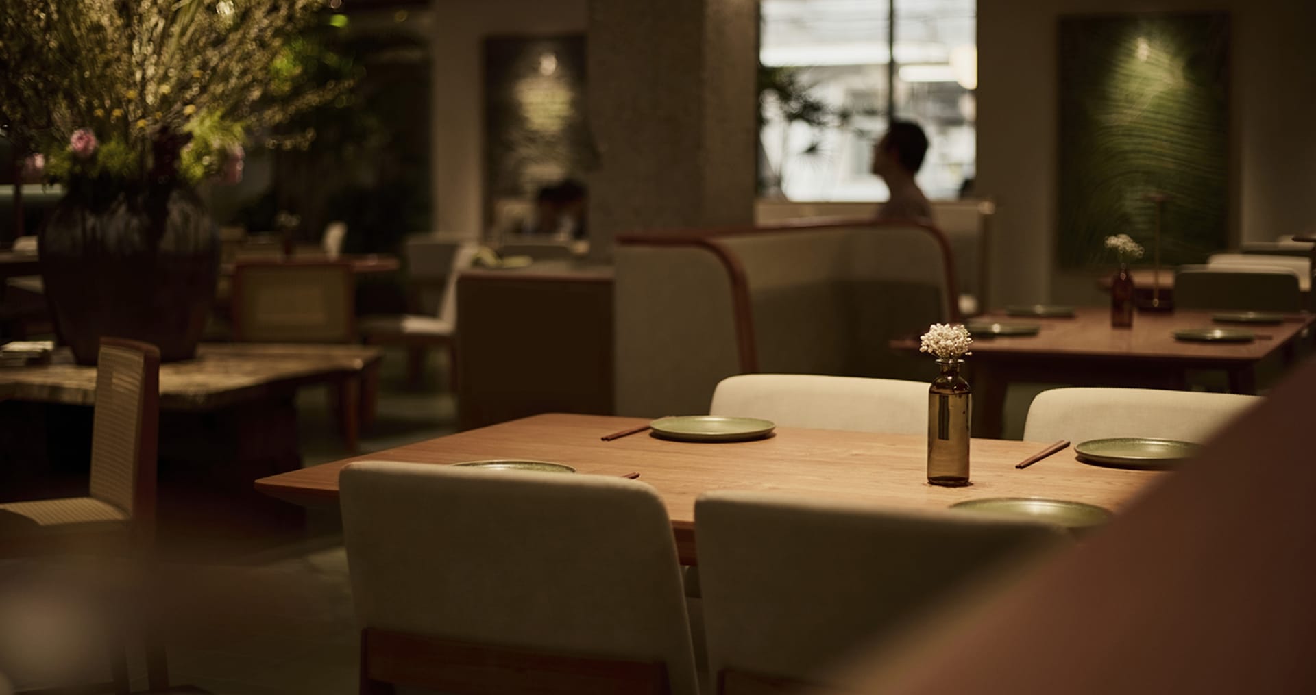 A calm and inviting restaurant with a wooden table and chairs, set with plates and a vase, in an empty space