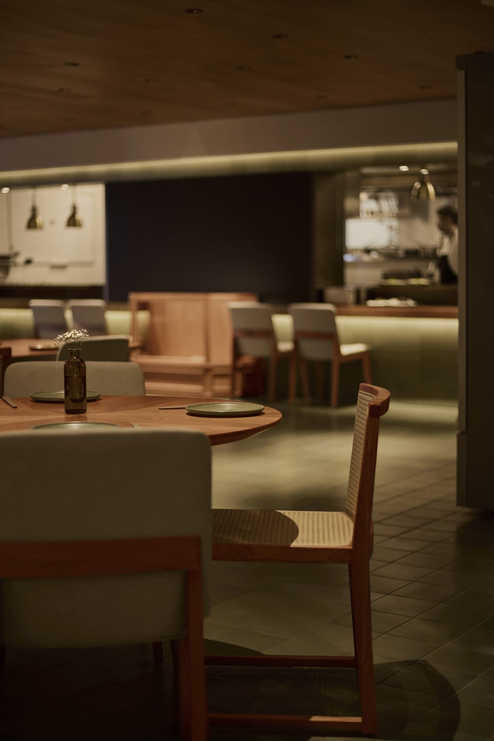 A dimly lit restaurant dining area with a large wooden table and metal chairs, surrounded by plates, bowls, and a vase, creating a warm and inviting atmosphere